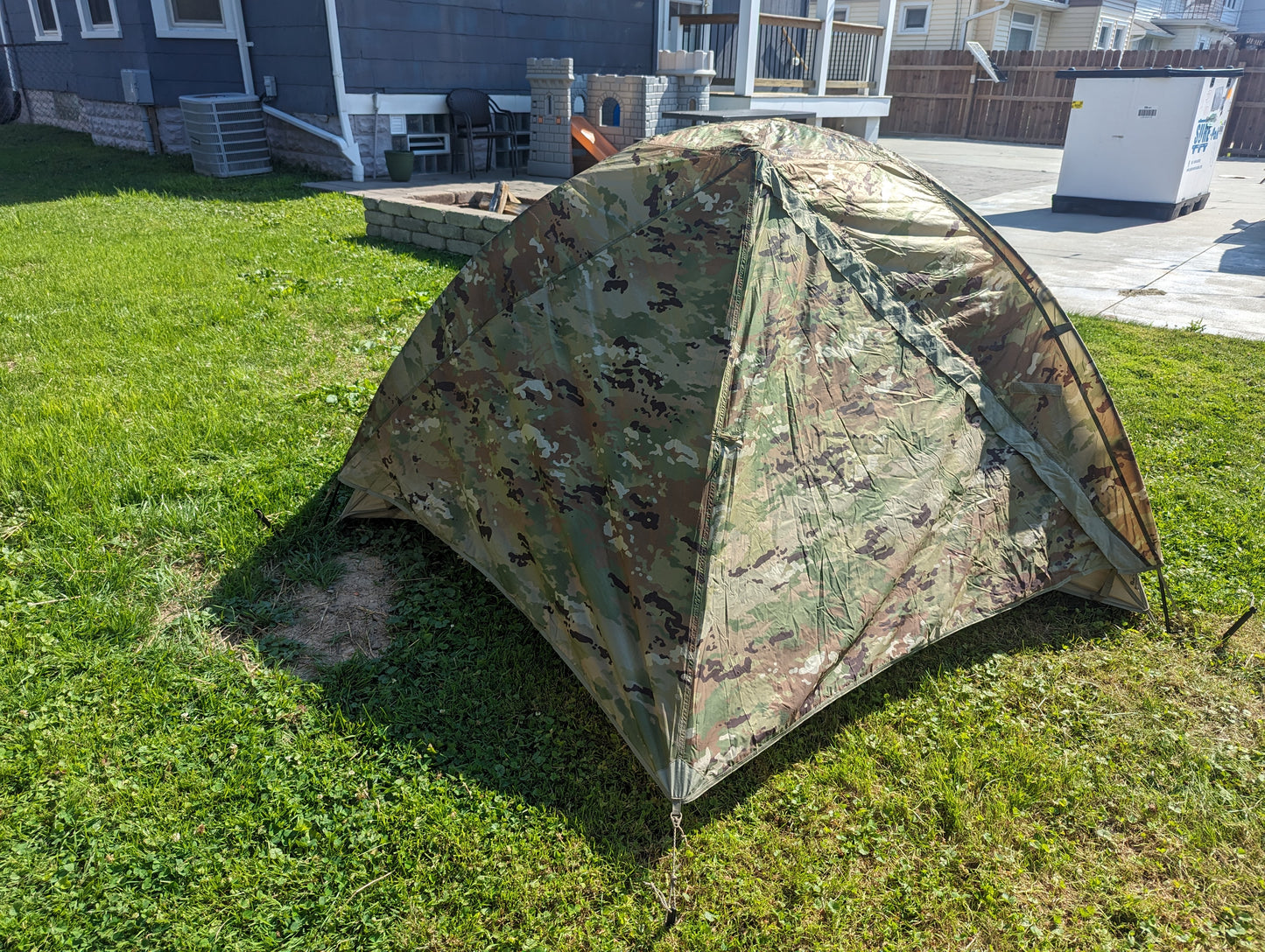A U.S. Military Litefighter 1-Man Combat Shelter in OCP/Multicam camouflage, fully pitched outdoors on a grassy lawn, displaying its low-profile, dome-like structure.