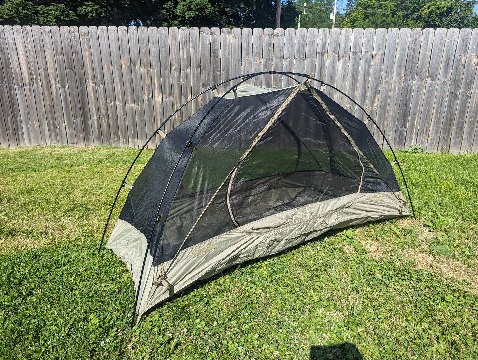 A U.S. Military Litefighter 1-Man Combat Shelter inner tent pitched outdoors on grass, featuring a black mesh canopy and tan nylon floor, highlighting the full structure without the rainfly.