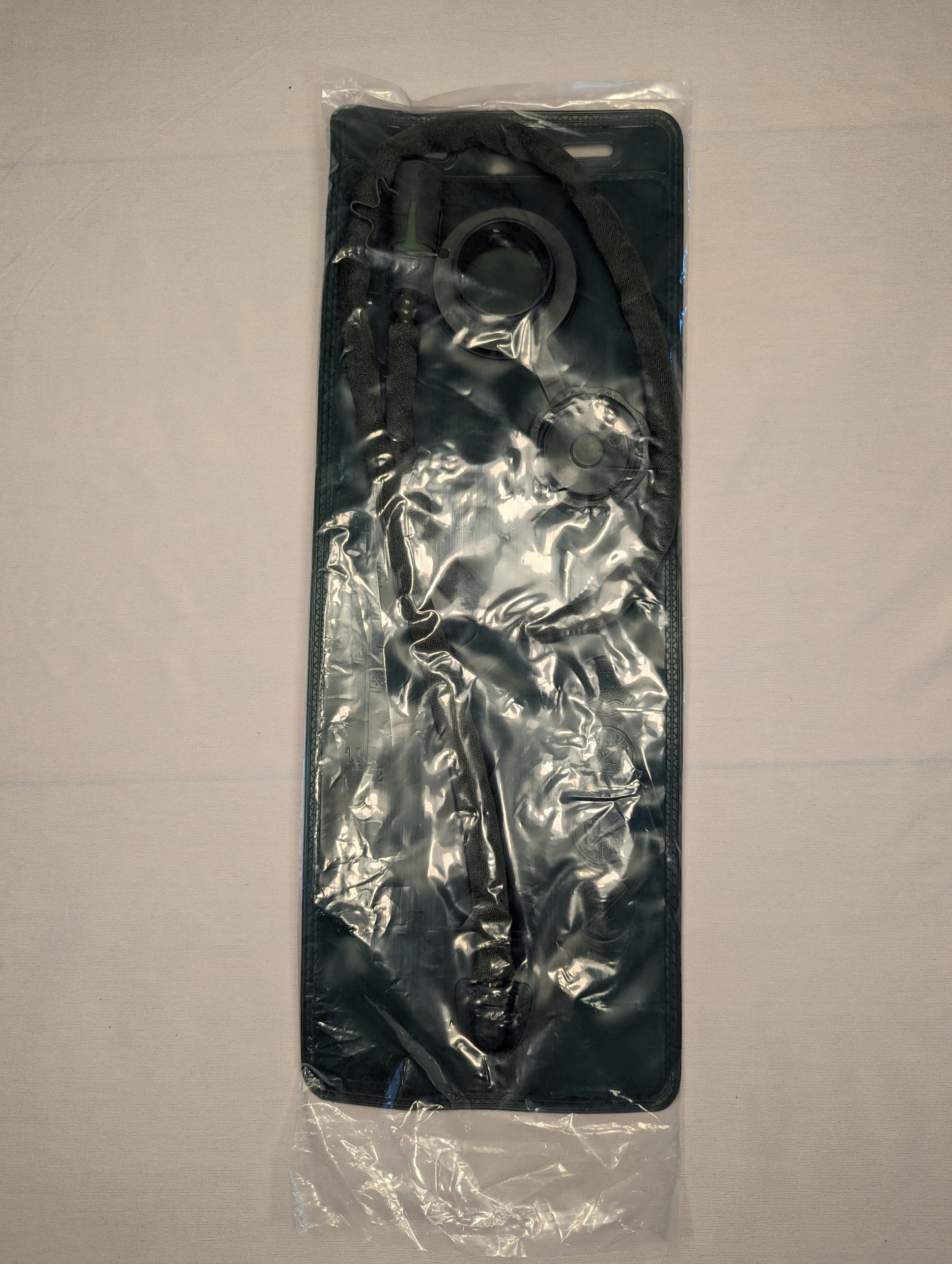 A new, black 3-Liter hydration bladder, hose, and bite valve assembly, sealed inside clear plastic packaging and laid on a light-colored background, indicating unused condition.