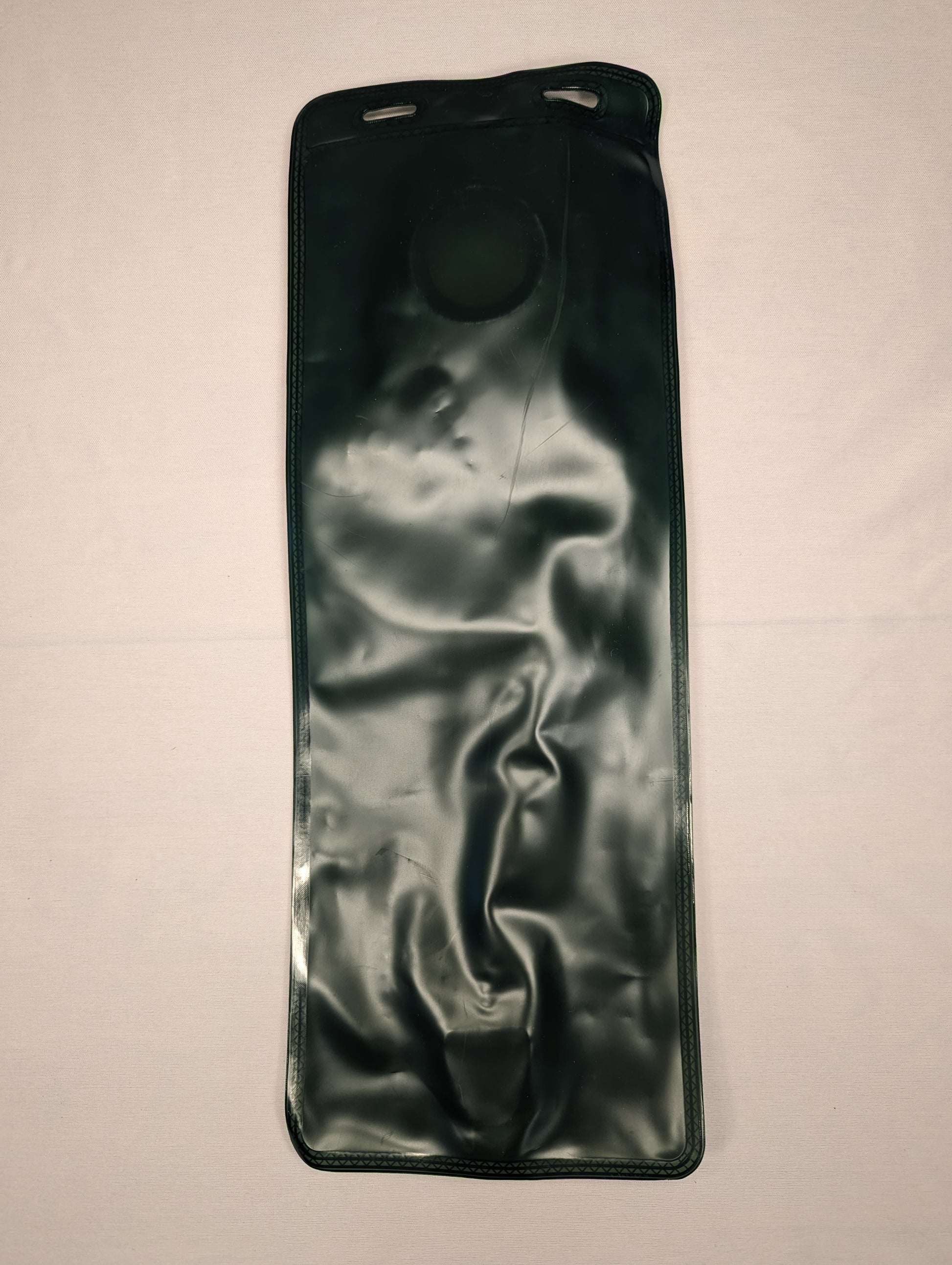 A full-length view of a new, dark green hydration bladder/reservoir, displaying the large circular filler cap and the flexible, crinkled material, laid flat on a light background.