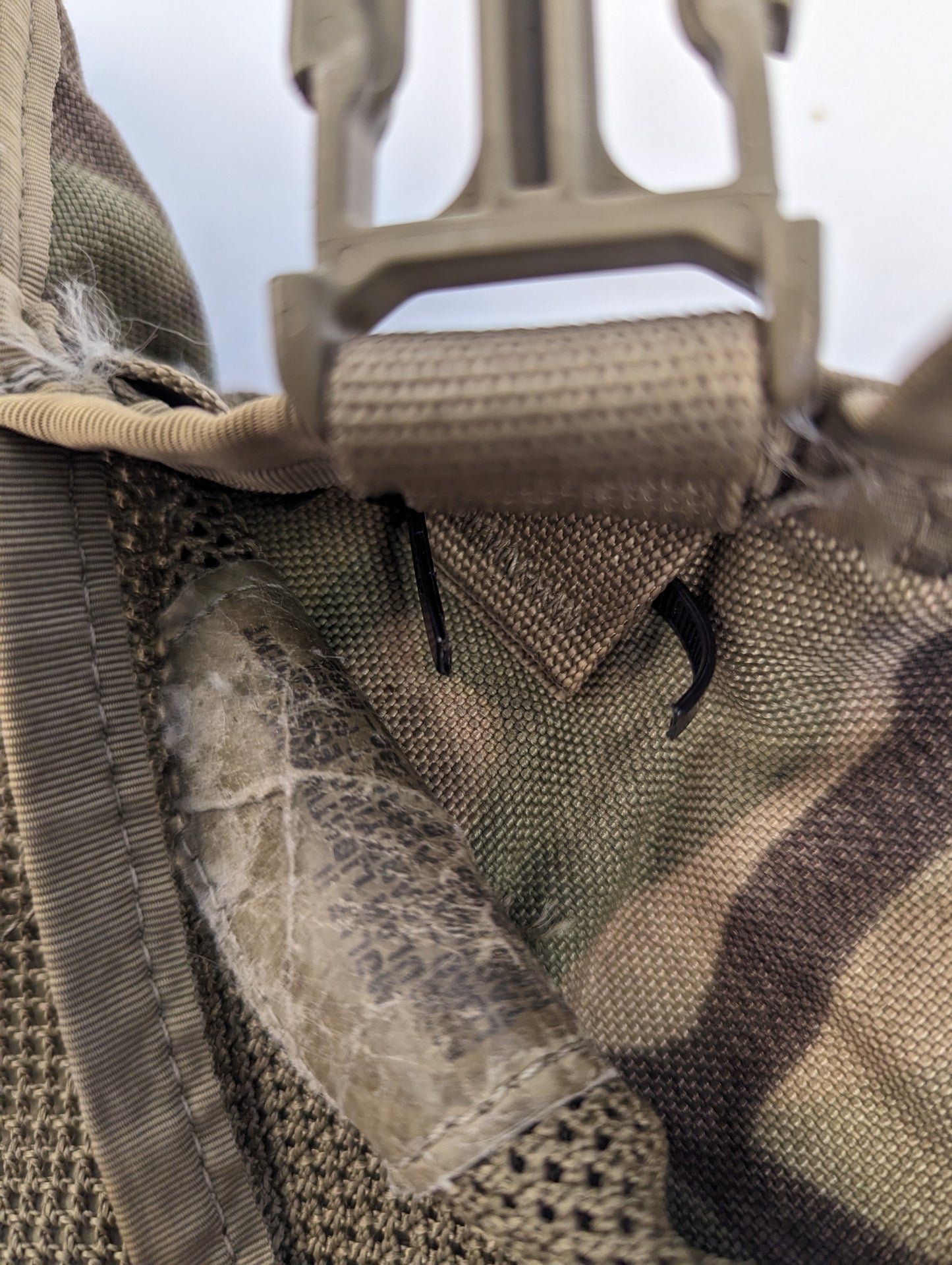 An extreme close-up of a U.S. Military OCP/Multicam pack, highlighting a tan quick-release buckle, heavy stitching, and significant peeling and abrasion on the camouflage fabric.