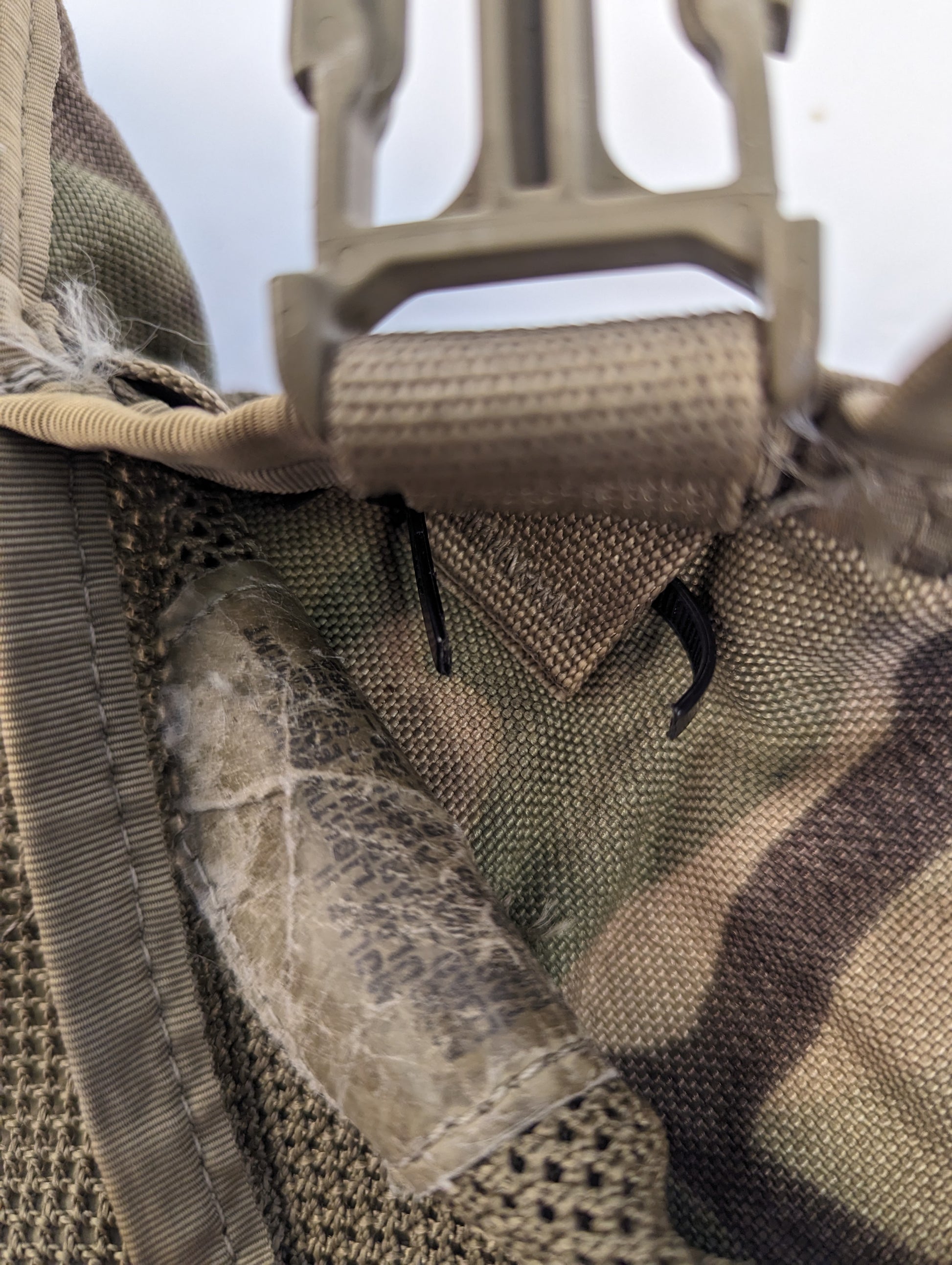 An extreme close-up of a U.S. Military OCP/Multicam pack, highlighting a tan quick-release buckle, heavy stitching, and significant peeling and abrasion on the camouflage fabric.