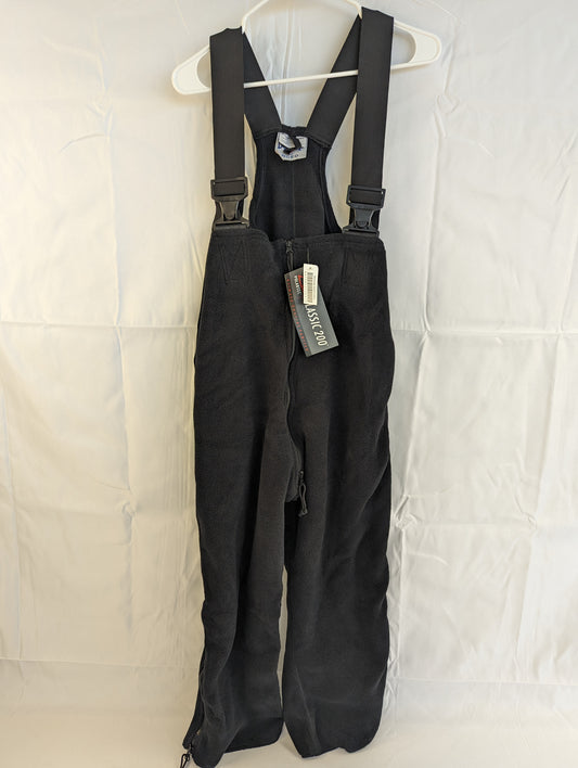 A full front view of black Polartec fleece cold weather overalls hanging on a hanger, featuring adjustable shoulder straps with buckles and the original tag attached.