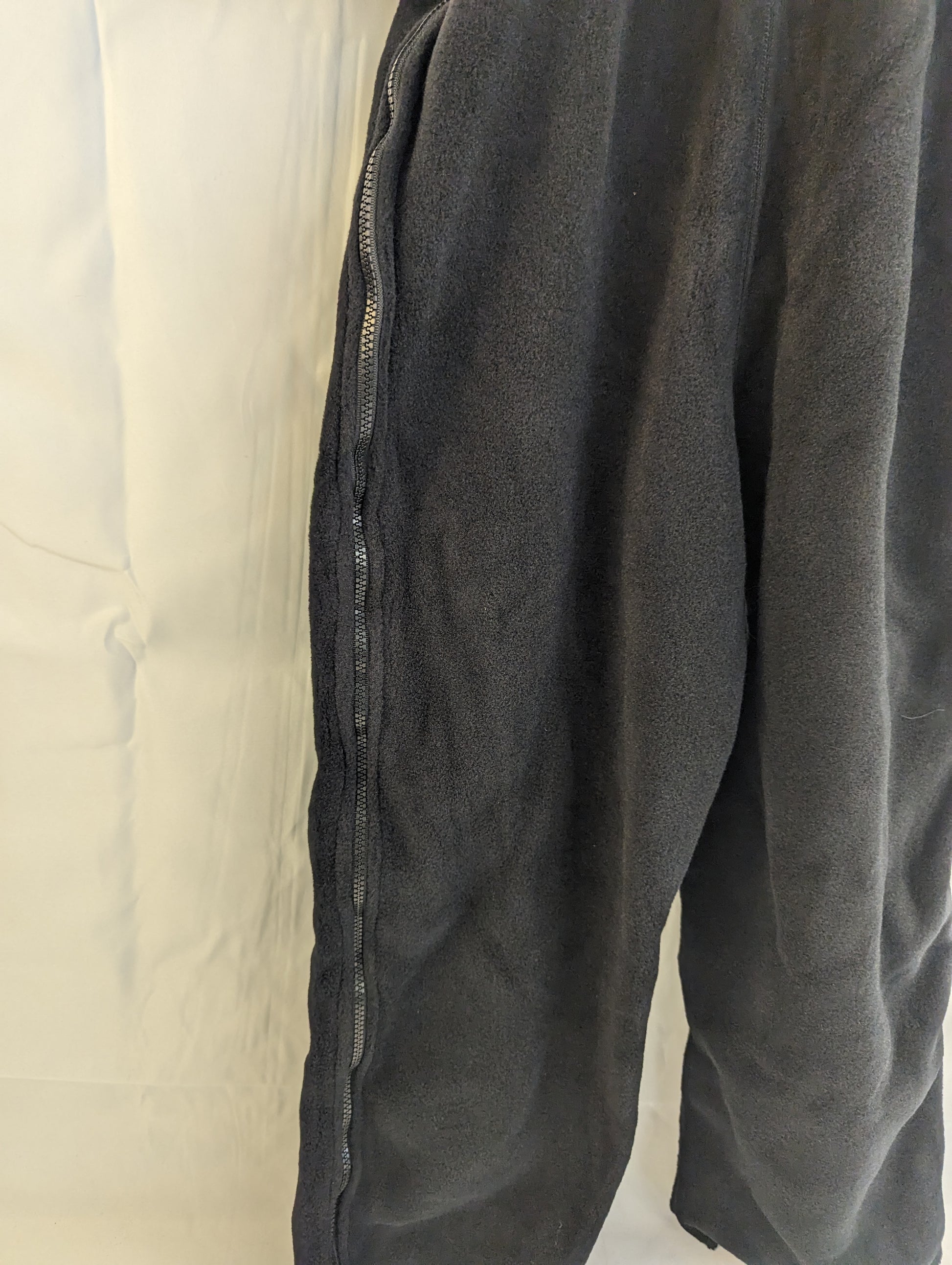A close-up view of the side zipper on the leg of black Polartec fleece cold weather overalls, highlighting the zipper mechanism and the texture of the black fleece fabric.