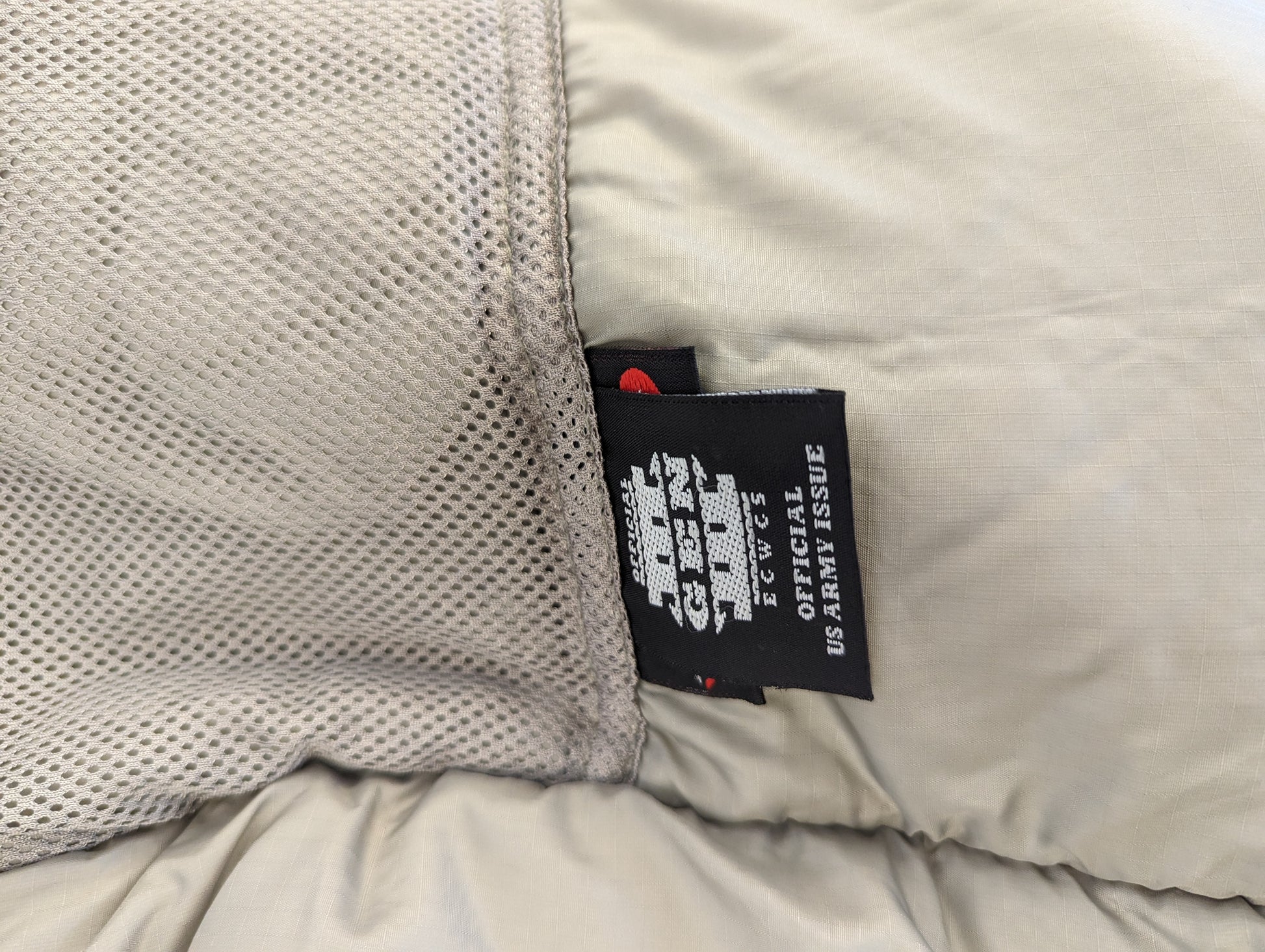 A close-up photograph of the black official U.S. Army issue tag sewn into the Extreme Cold Weather Parka, prominently displaying 'ECWCS GEN III', 'OFFICIAL U.S. ARMY ISSUE', and 'Made in U.S.A.' branding.