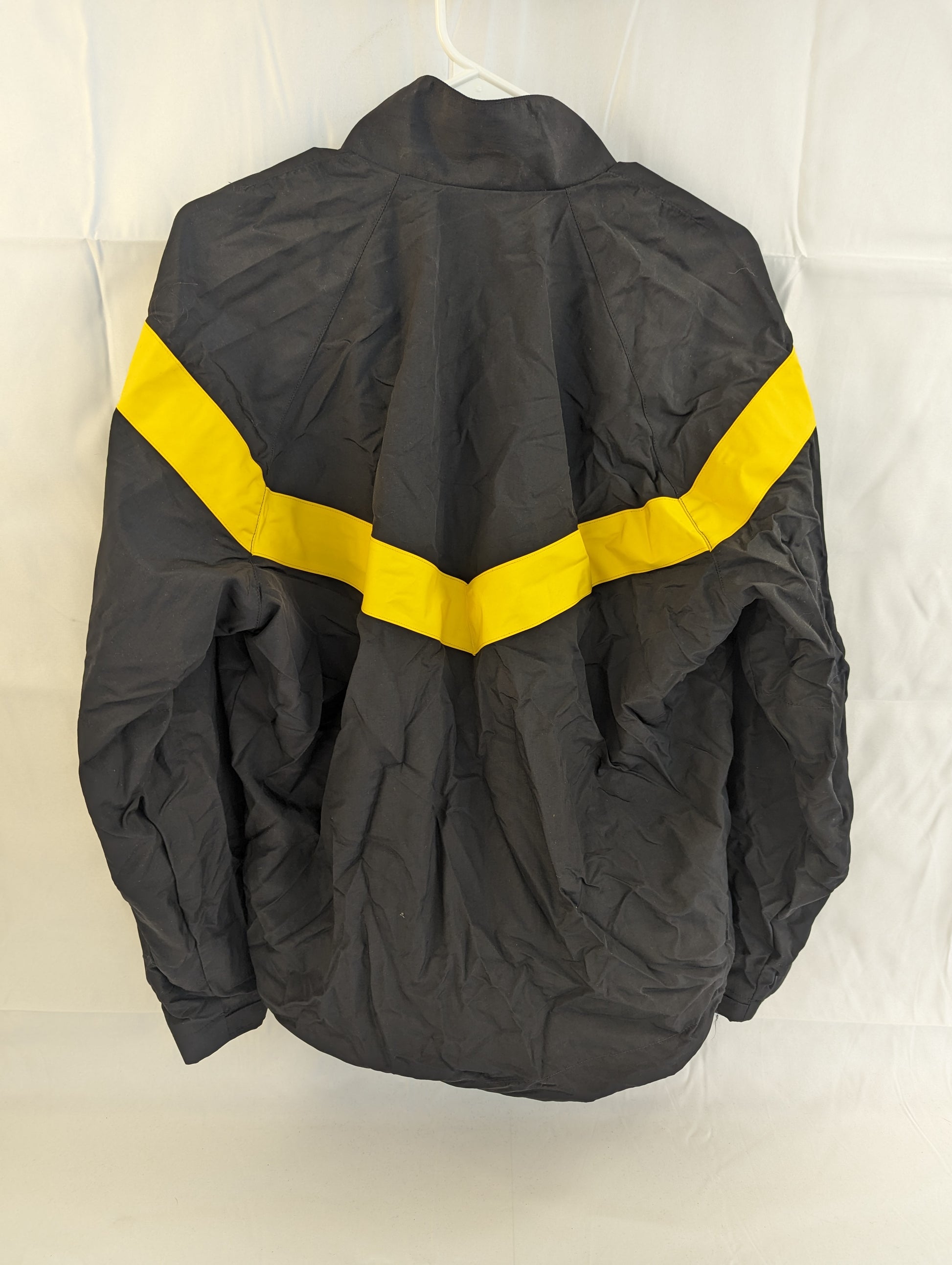 A back view of a black U.S. Army Physical Training (PT) jacket hanging on a hanger, featuring a bold yellow chevron stripe across the upper back.