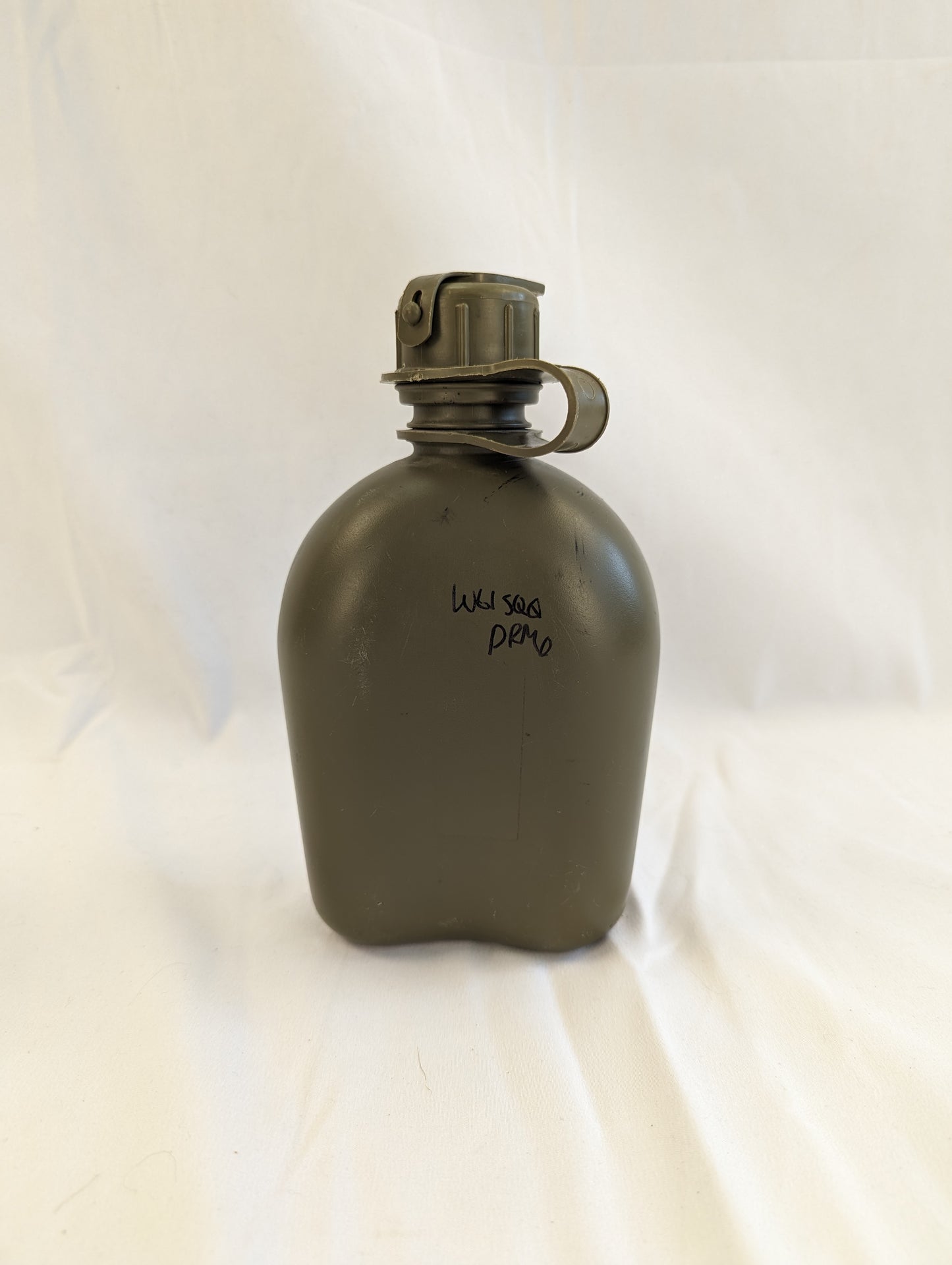 A close-up studio shot of a used U.S. Military Surplus 1-quart plastic canteen in olive green with a black cap, showing faint molded text and a visible handwritten military stock number.