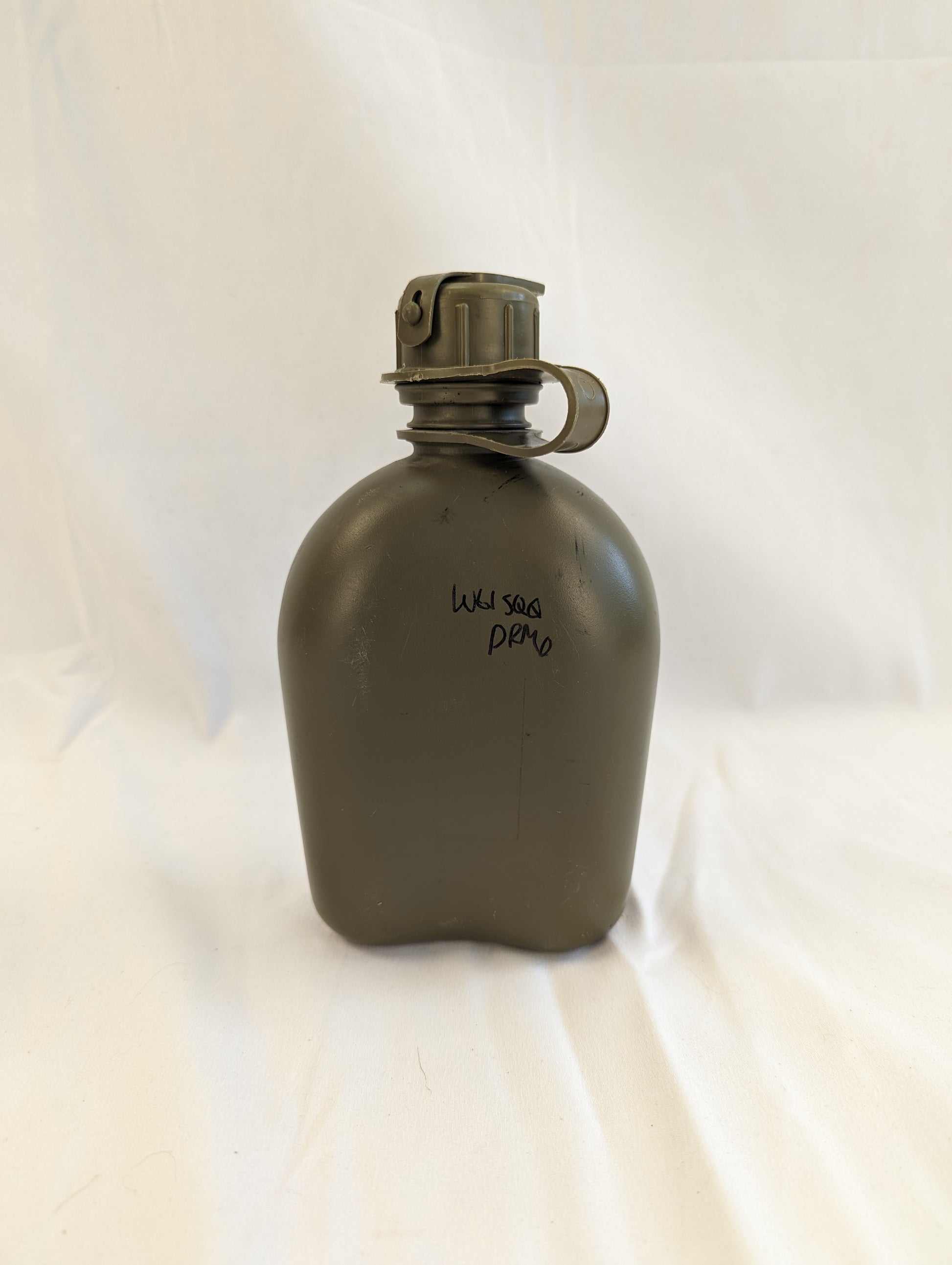 A close-up studio shot of a used U.S. Military Surplus 1-quart plastic canteen in olive green with a black cap, showing faint molded text and a visible handwritten military stock number.