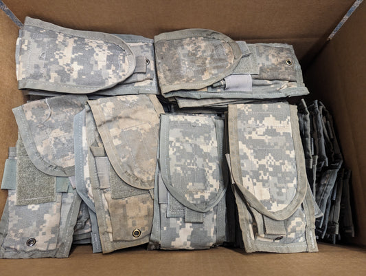 A cardboard box filled with approximately one hundred stacked and folded U.S. Military Surplus 2-Mag Pouches in ACU digital camouflage.