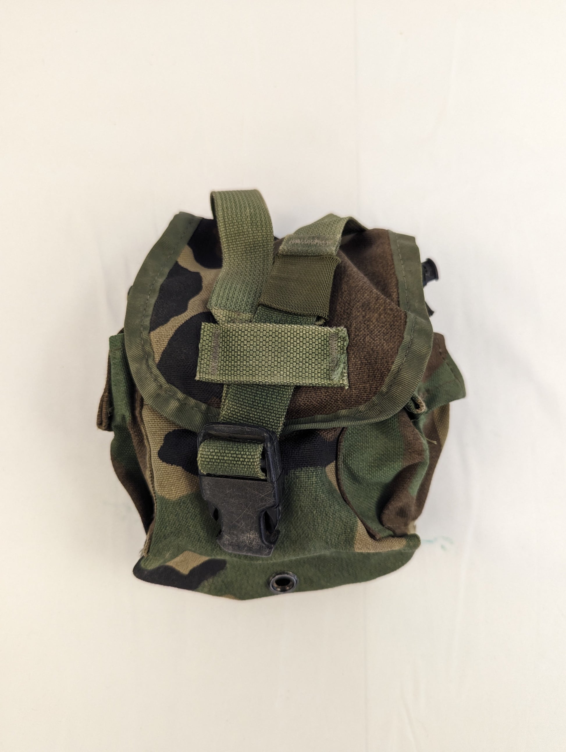 A single U.S. Military Surplus 1-Quart Canteen Pouch in Woodland camouflage, standing upright, with the flap closed and secured by a vertical webbing strap and black quick-release buckle.