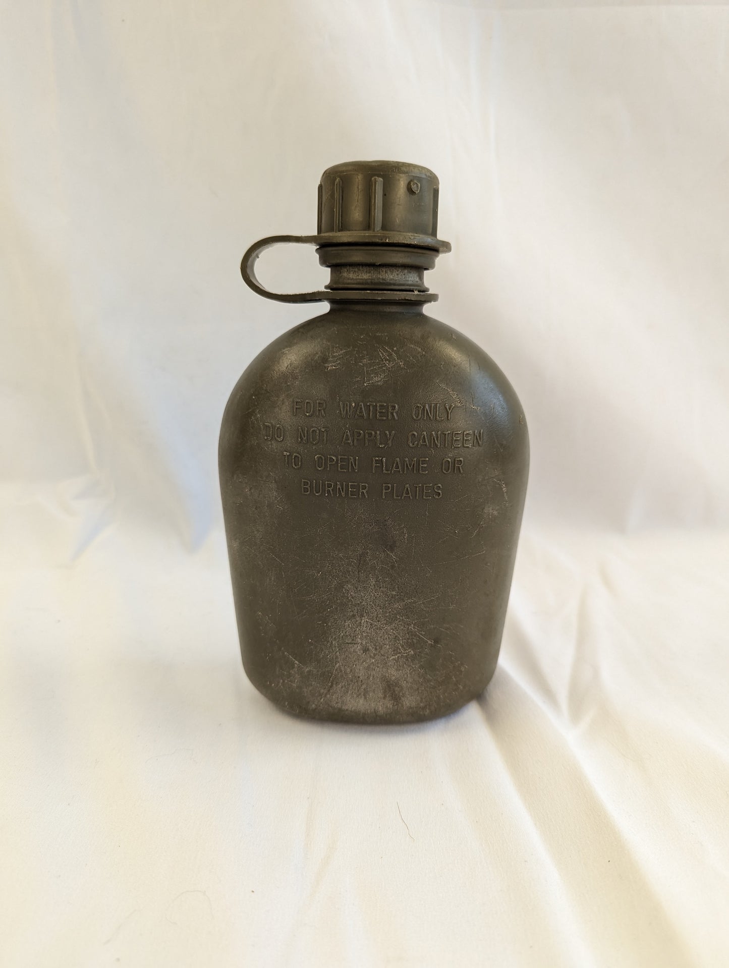 A single U.S. Military 1-quart canteen made of dark, aged metal, standing upright on a white background, featuring embossed military markings and a tethered screw cap.