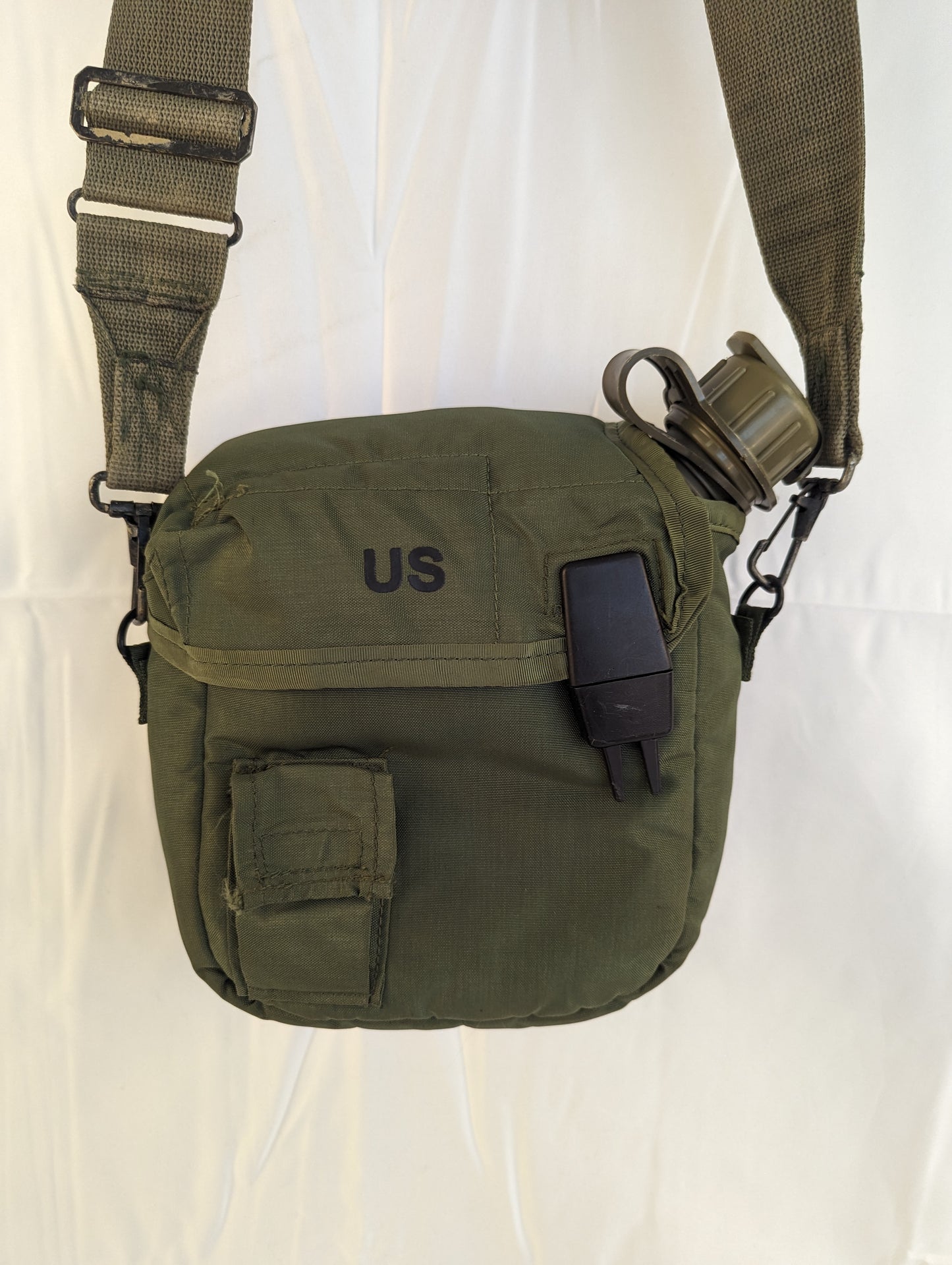 A U.S. Military Surplus 2-quart collapsible water canteen in an olive green cover with a shoulder sling strap, featuring a small utility pocket, a plastic buckle closure, and a stenciled 'US' marking on the front.