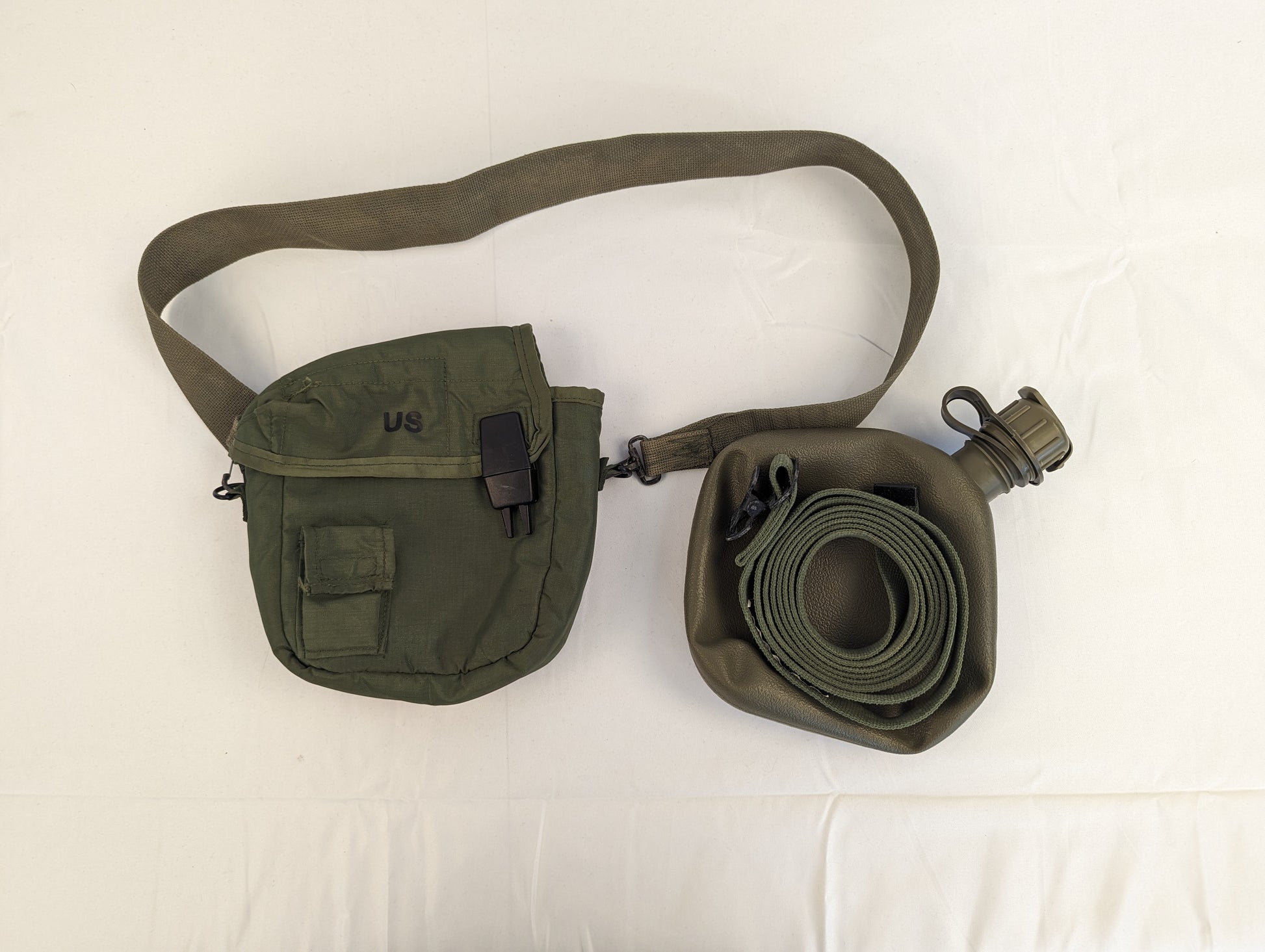A U.S. Military Surplus 2-quart collapsible water canteen set, displaying the olive green nylon cover with 'US' marking and shoulder sling next to the collapsible bladder and cap on a white background.