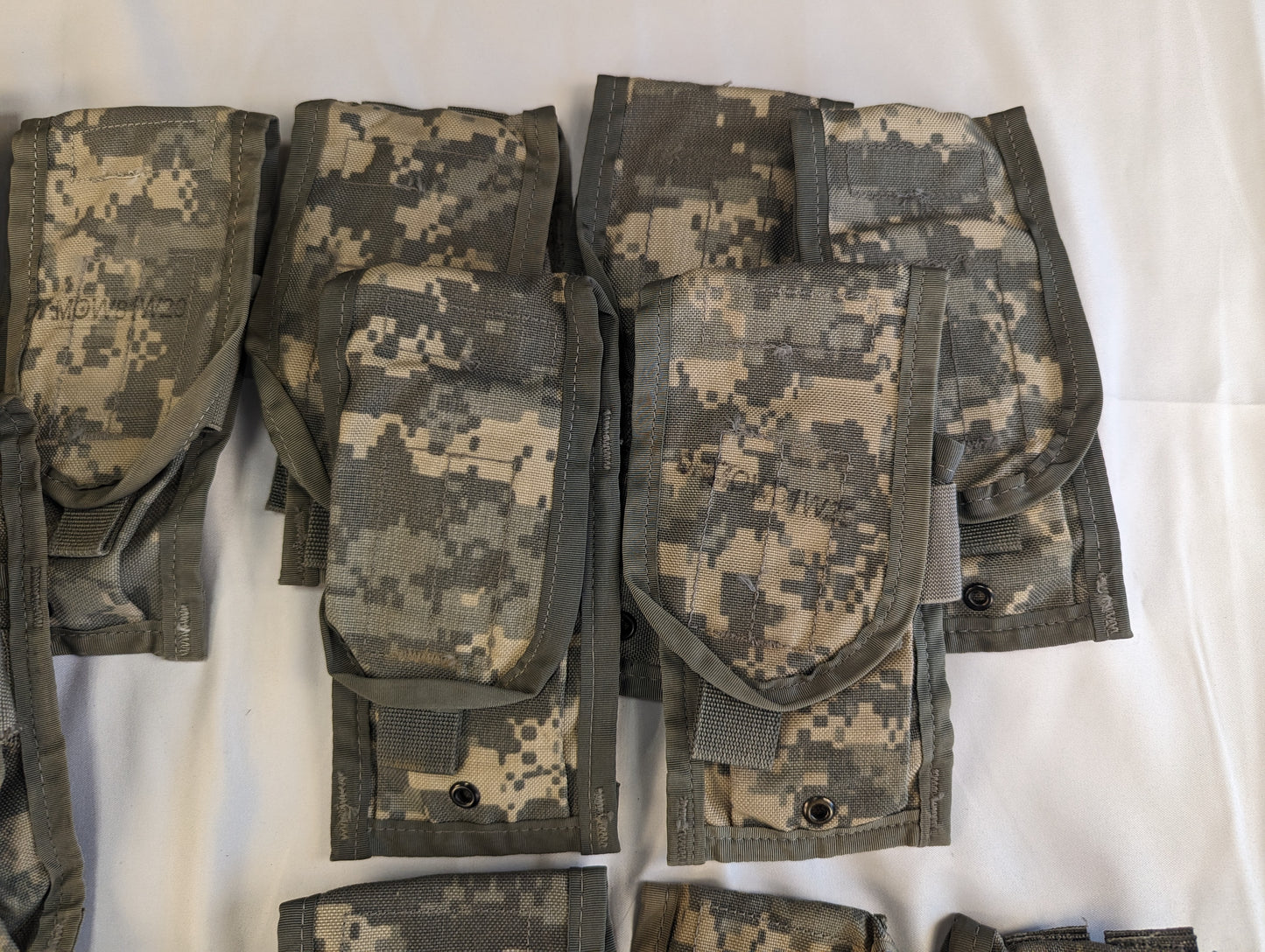 A close-up studio shot of a cluster of overlapping U.S. Military Surplus 2-Mag Pouches in ACU digital camouflage, highlighting the flaps, snap closures, and worn fabric texture.