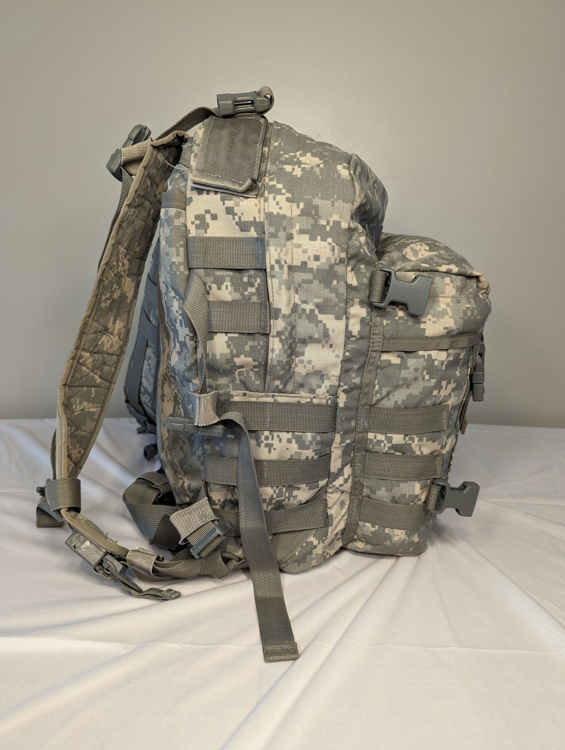 A slightly angled front view of a U.S. Military Surplus 3-Day Assault Pack in ACU digital camouflage, highlighting the padded shoulder straps, multiple compression straps, and horizontal MOLLE webbing.