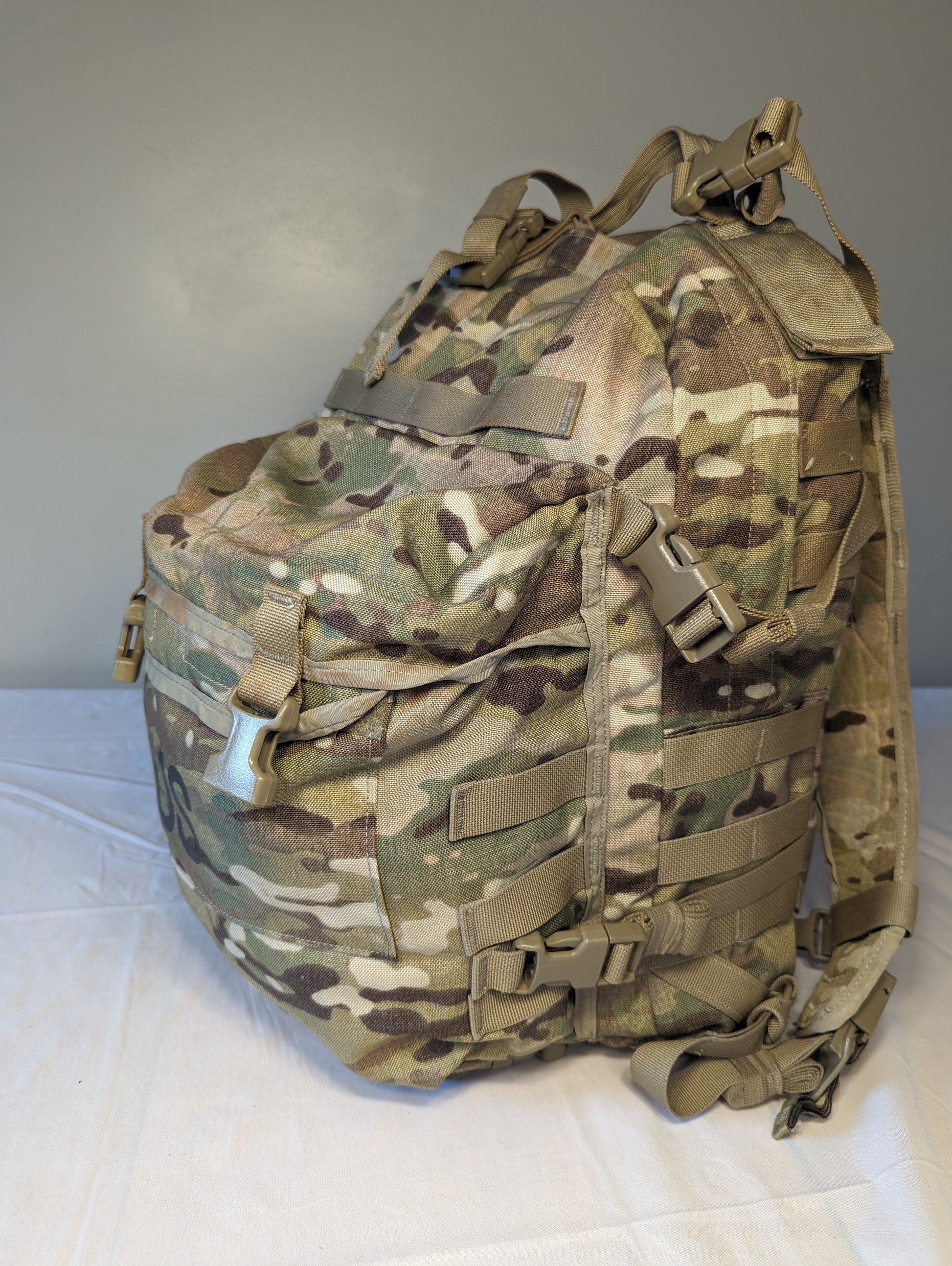 A front view of a U.S. Military Surplus 3-Day Assault Pack in OCP/Multicam camouflage, standing upright, featuring extensive horizontal MOLLE webbing, quick-release buckle closures, and padded shoulder straps.