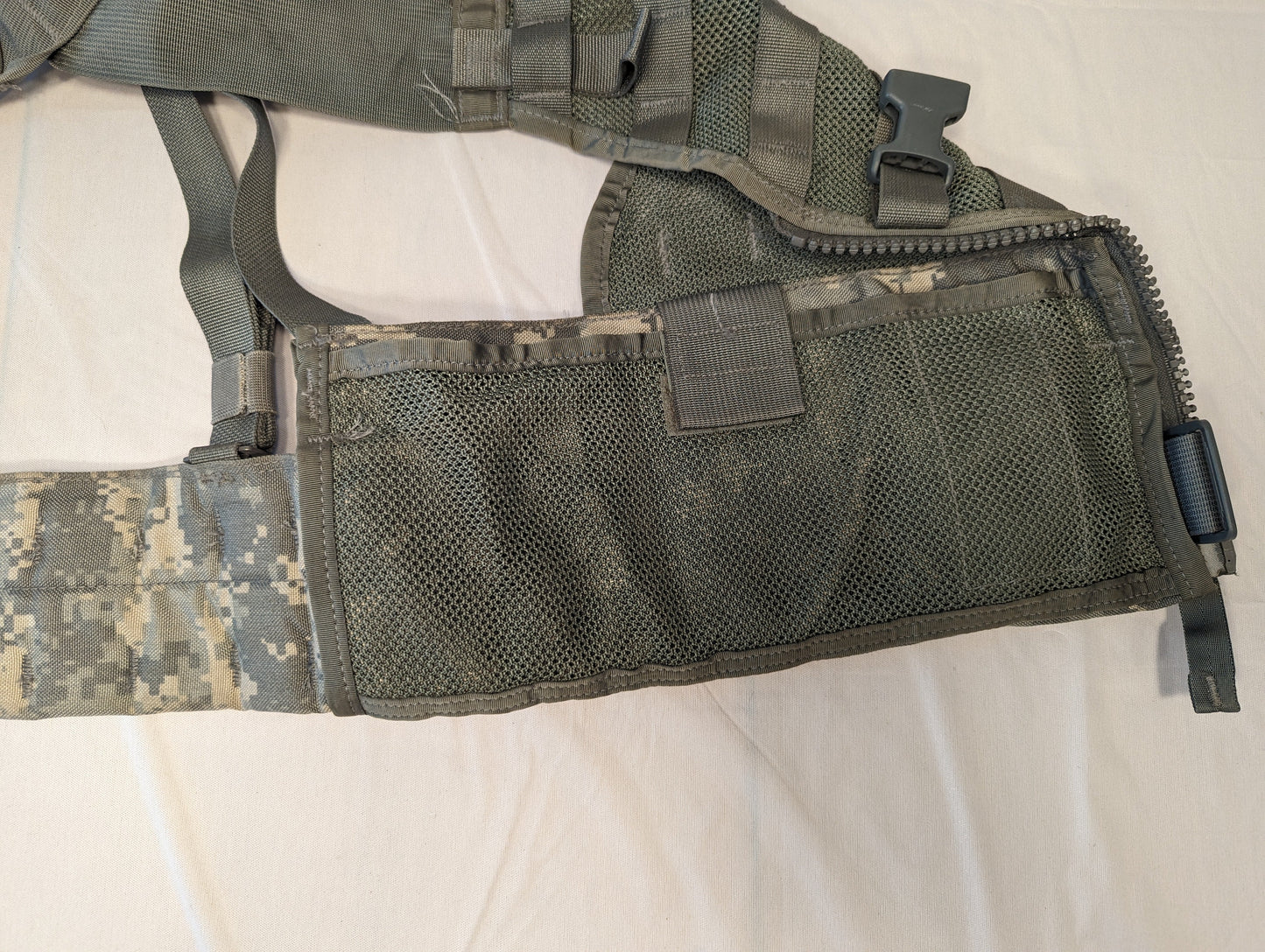 A close-up view of the side torso panel of the U.S. Military Load Carrier Vest (FLC), highlighting the breathable mesh body, the vertical zipper, and the quick-release adjustment buckle.