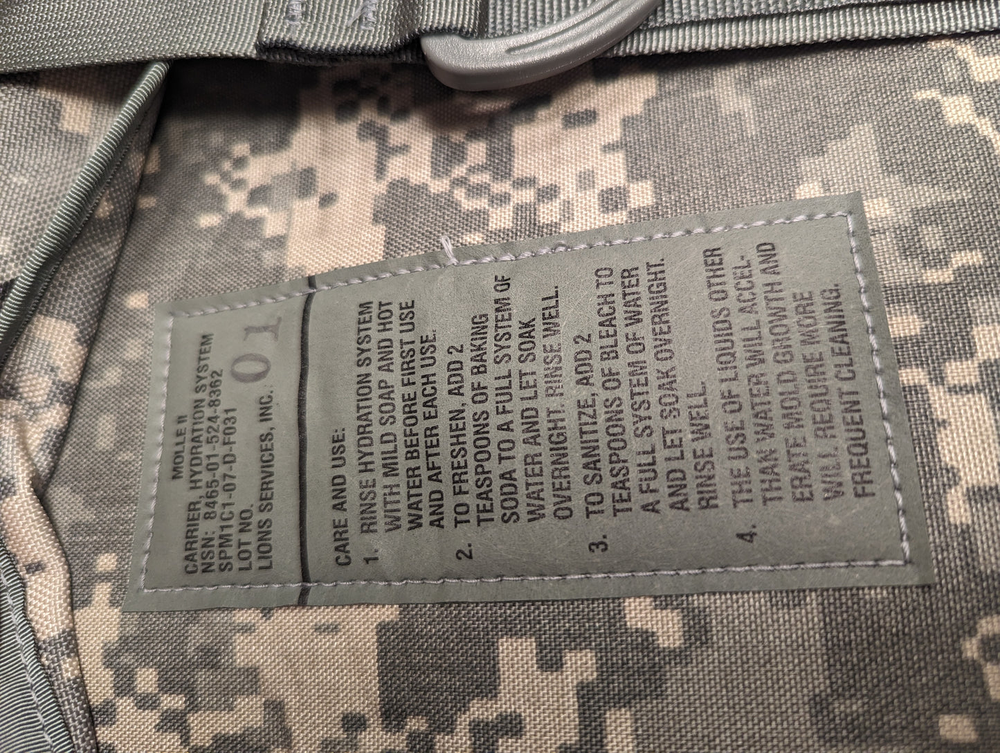 A close-up photograph of the U.S. Military Hydration Carrier care tag, displaying detailed instructions for cleaning and sanitizing the reservoir with soap, baking soda, and bleach, along with mildew warnings.