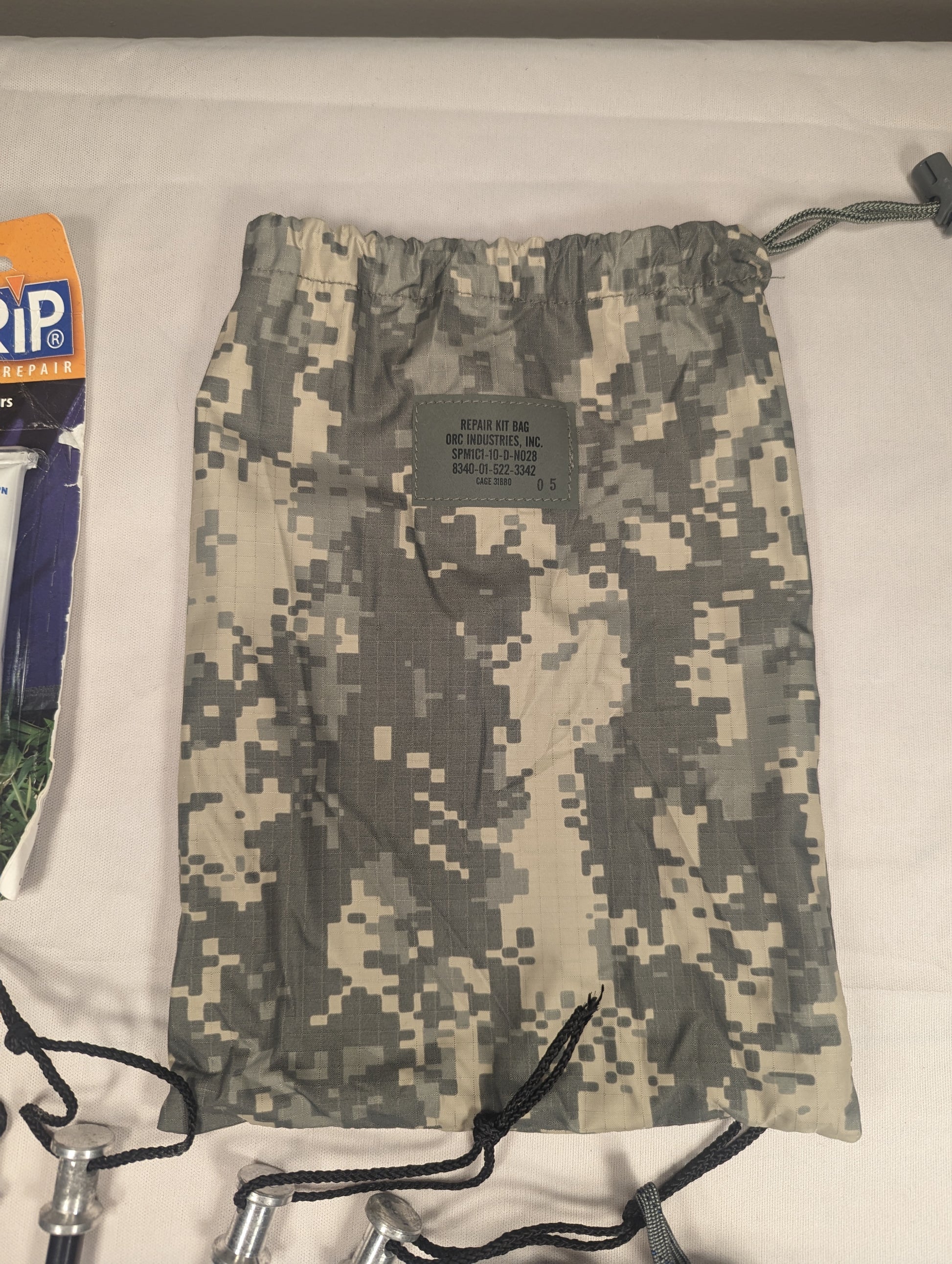 A U.S. Military Surplus ICS Tent Repair Kit drawstring bag in ACU digital camouflage, featuring a cinched closure and an official issue label sewn onto the front.