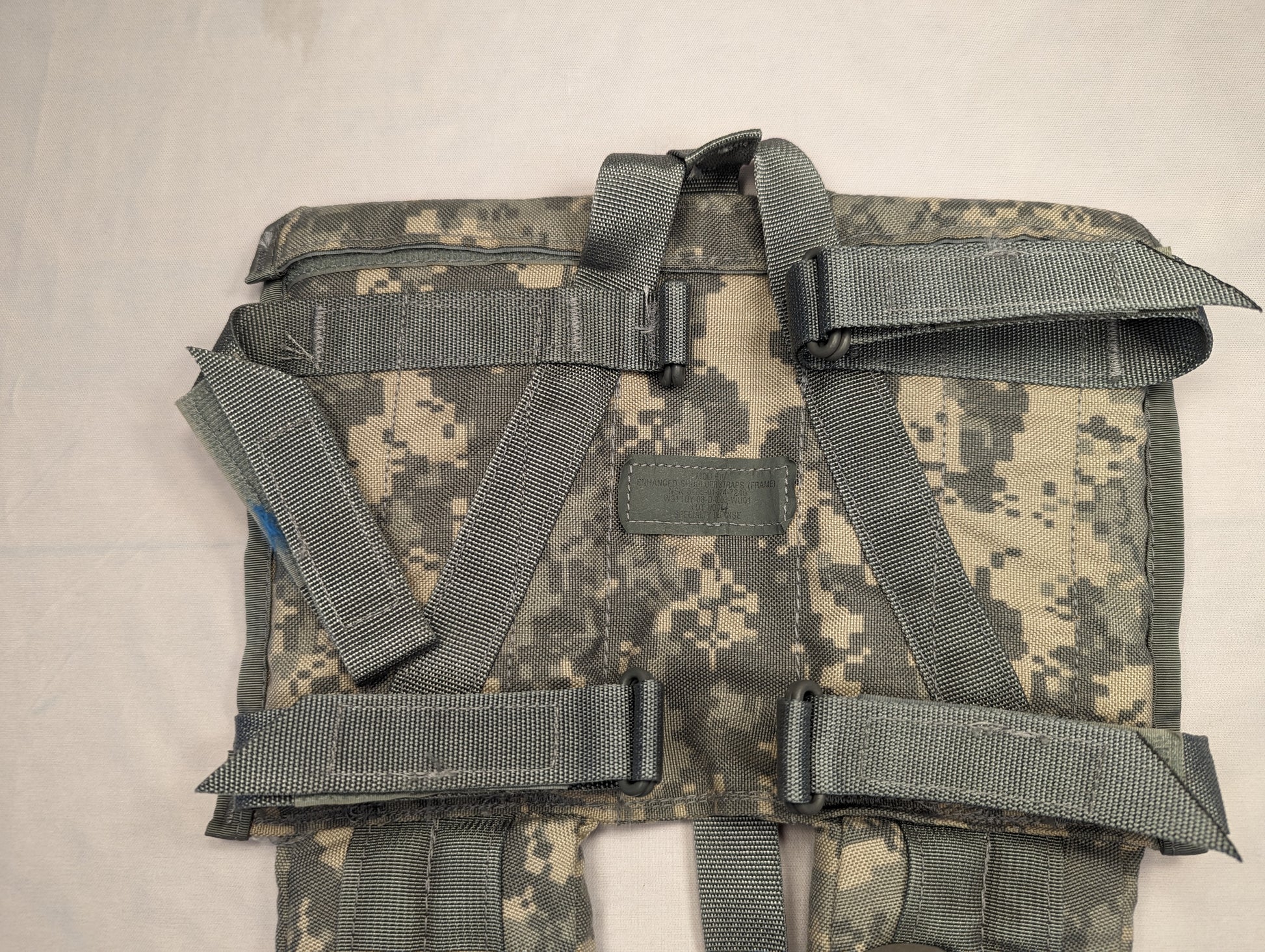 A close-up view of the interior back panel of a U.S. Military ACU digital camouflage load-bearing straps, displaying the complex arrangement of gray webbing adjustment straps and a central identification patch field.