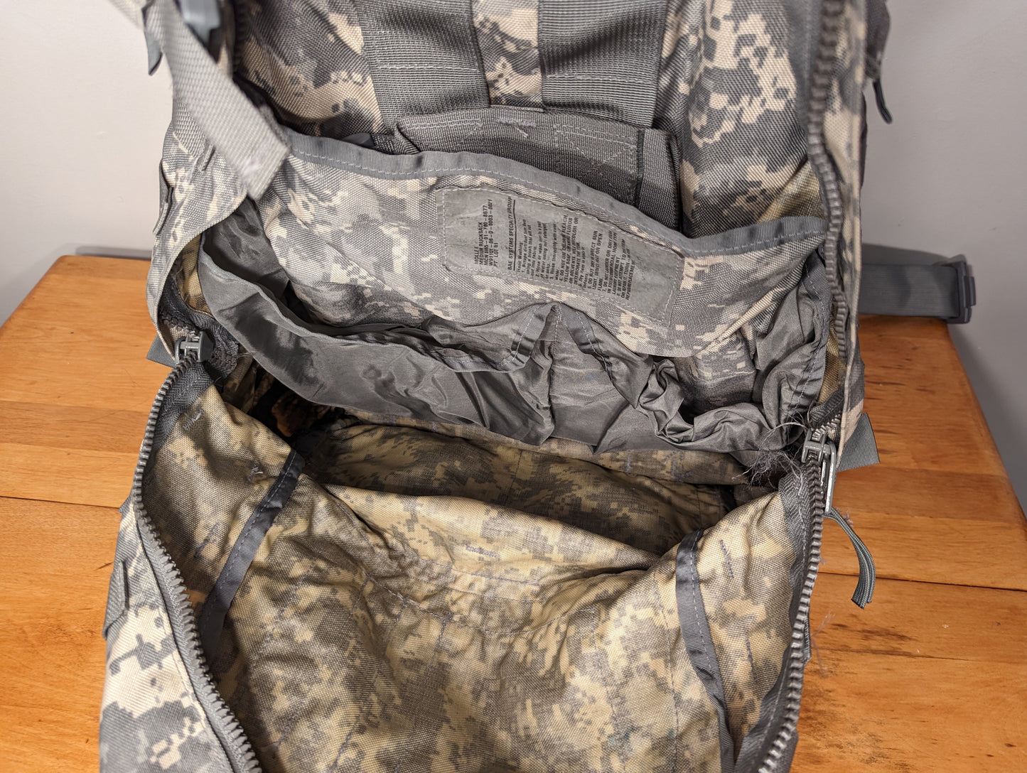 A close-up view looking into the open main compartment of the U.S. Military Medium Field Pack in ACU digital camouflage, highlighting the drawstring collar, multiple internal organizational sleeves, and the pack's soiled, used interior lining.
