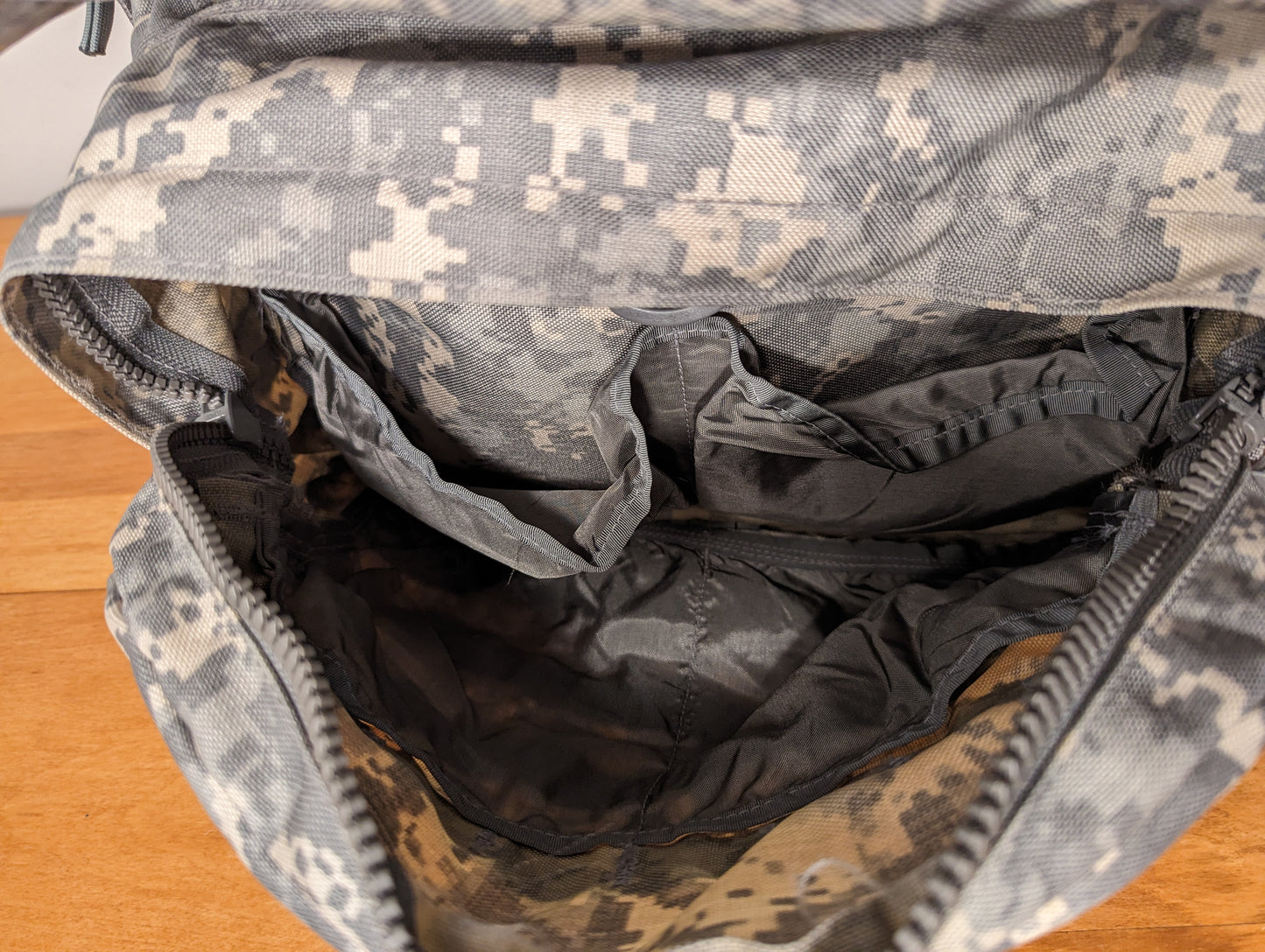 A close-up view looking into the open main compartment of the U.S. Military Medium Field Pack in ACU digital camouflage, highlighting the drawstring collar and multiple internal organizational sleeves and mesh pockets.