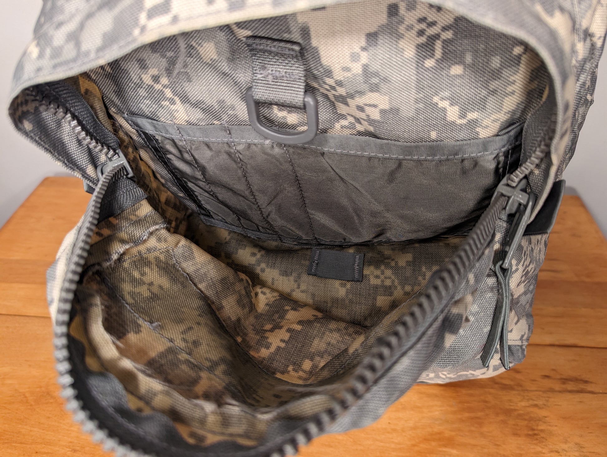 A close-up view looking into the open main compartment of the U.S. Military Medium Field Pack in ACU digital camouflage, highlighting the drawstring collar and internal mesh pocket.