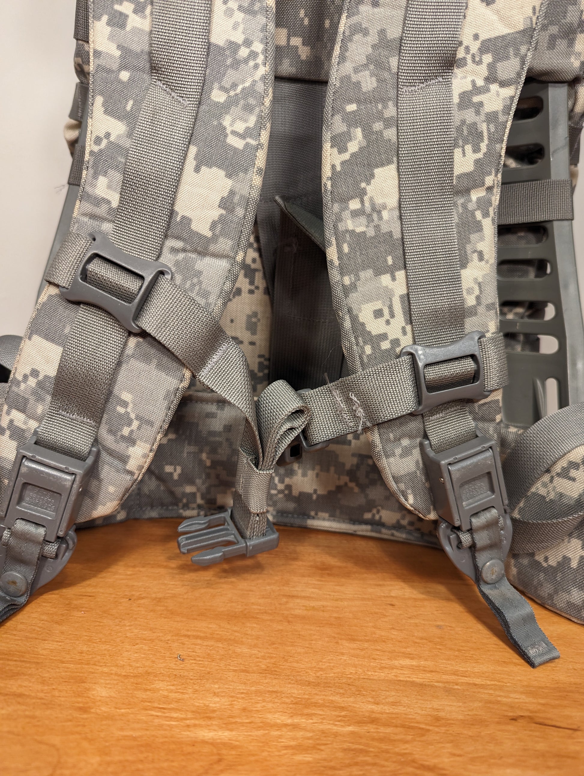 A close-up view of the back suspension system on a U.S. Military Medium Field Pack in ACU digital camouflage, highlighting the padded shoulder straps, black buckles, and rigid frame.