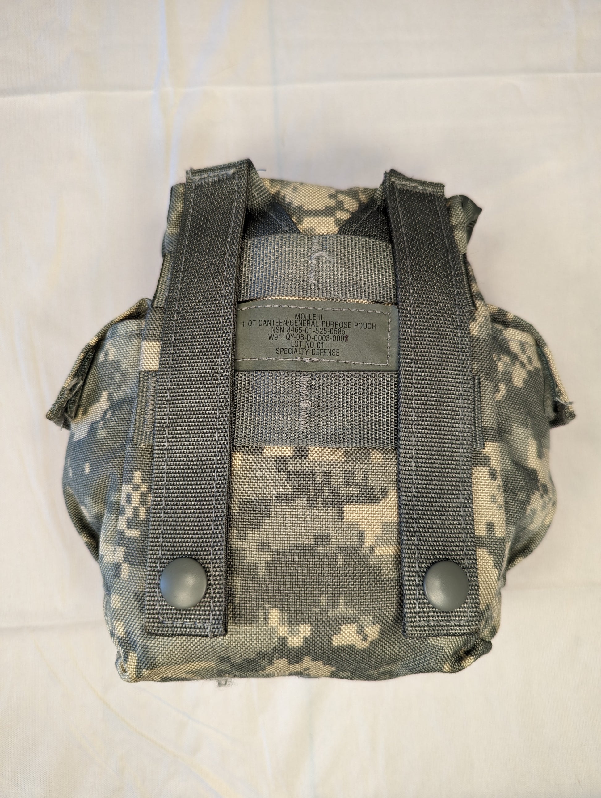 A close-up photograph of the back view of a U.S. Military Surplus Canteen/General Purpose Pouch in ACU digital camouflage, clearly displaying the two vertical MOLLE attachment straps, snap buttons, and the issue label.