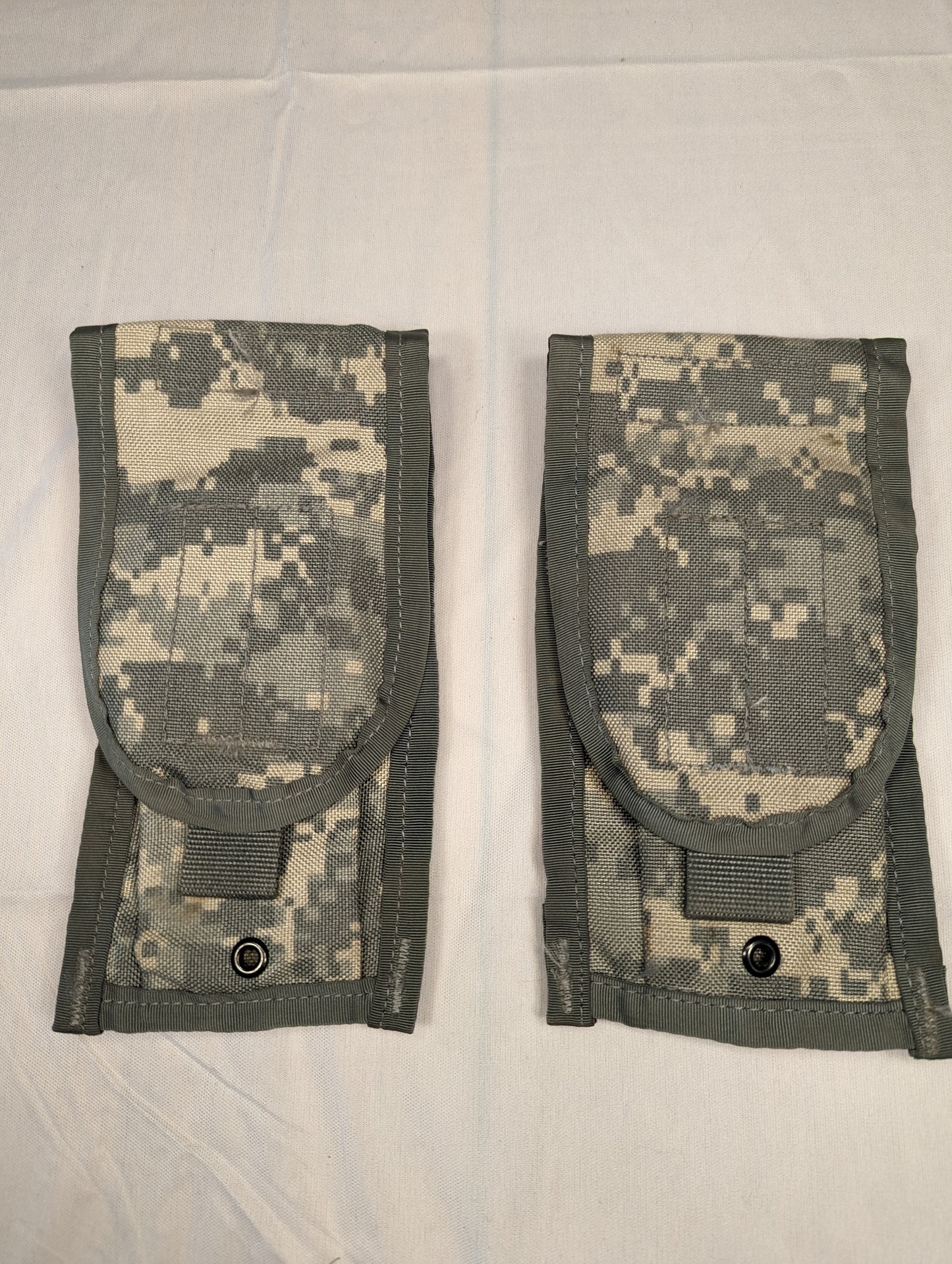 A pair of U.S. Military Surplus Double Magazine Pouches in ACU digital camouflage, laid side-by-side, featuring flap closures secured by black metal snap buttons and vertical webbing.