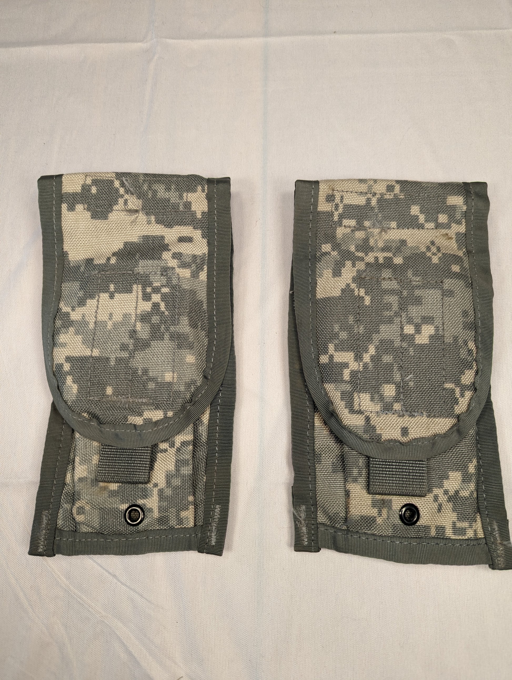 A pair of U.S. Military Surplus Double Magazine Pouches in ACU digital camouflage, laid side-by-side, featuring flap closures secured by black metal snap buttons and vertical webbing.