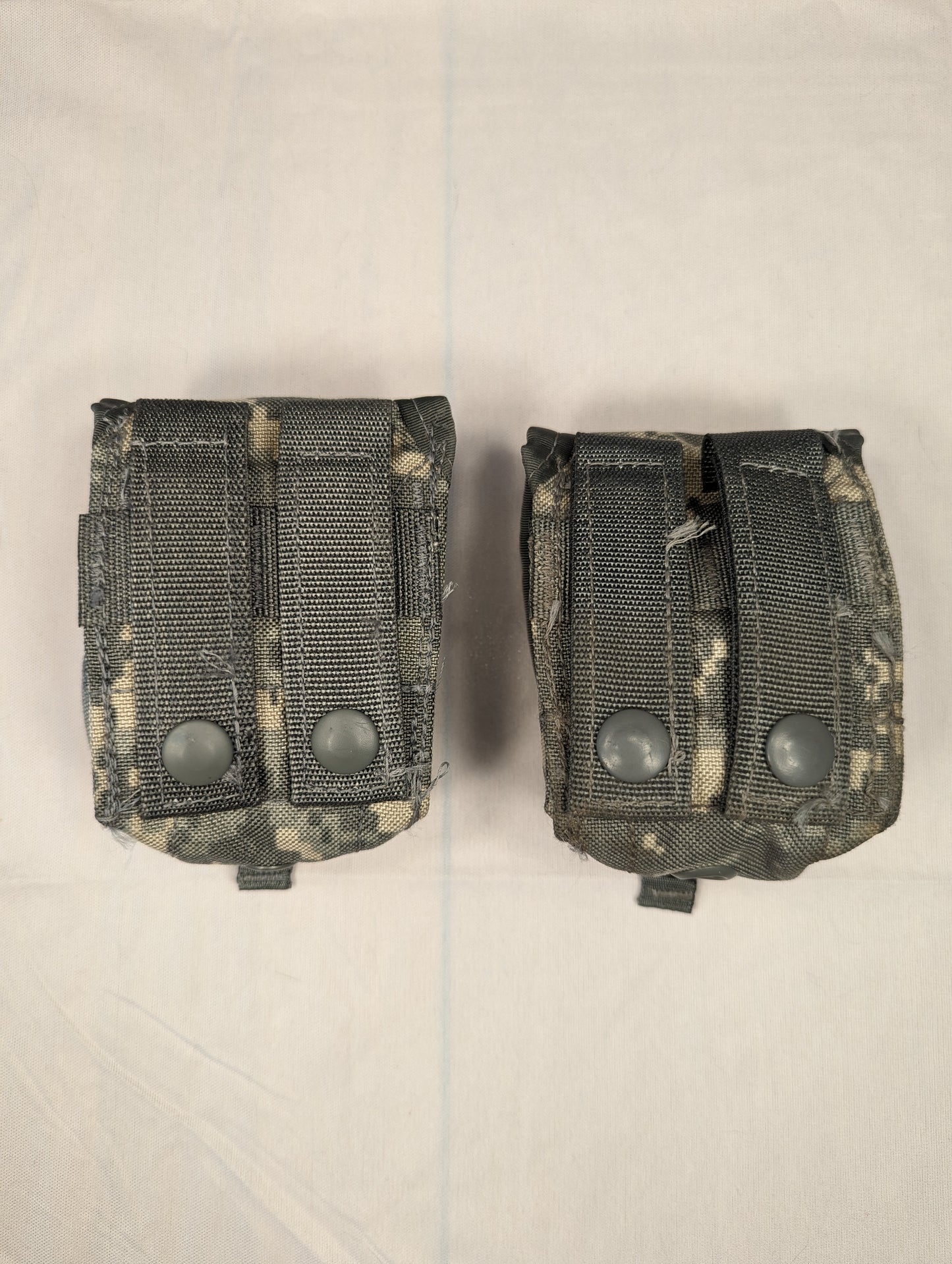 A close-up studio shot of two U.S. Military Surplus Double Magazine Pouches in ACU digital camouflage, laid side-by-side, featuring dense horizontal MOLLE webbing and snap-button flaps.