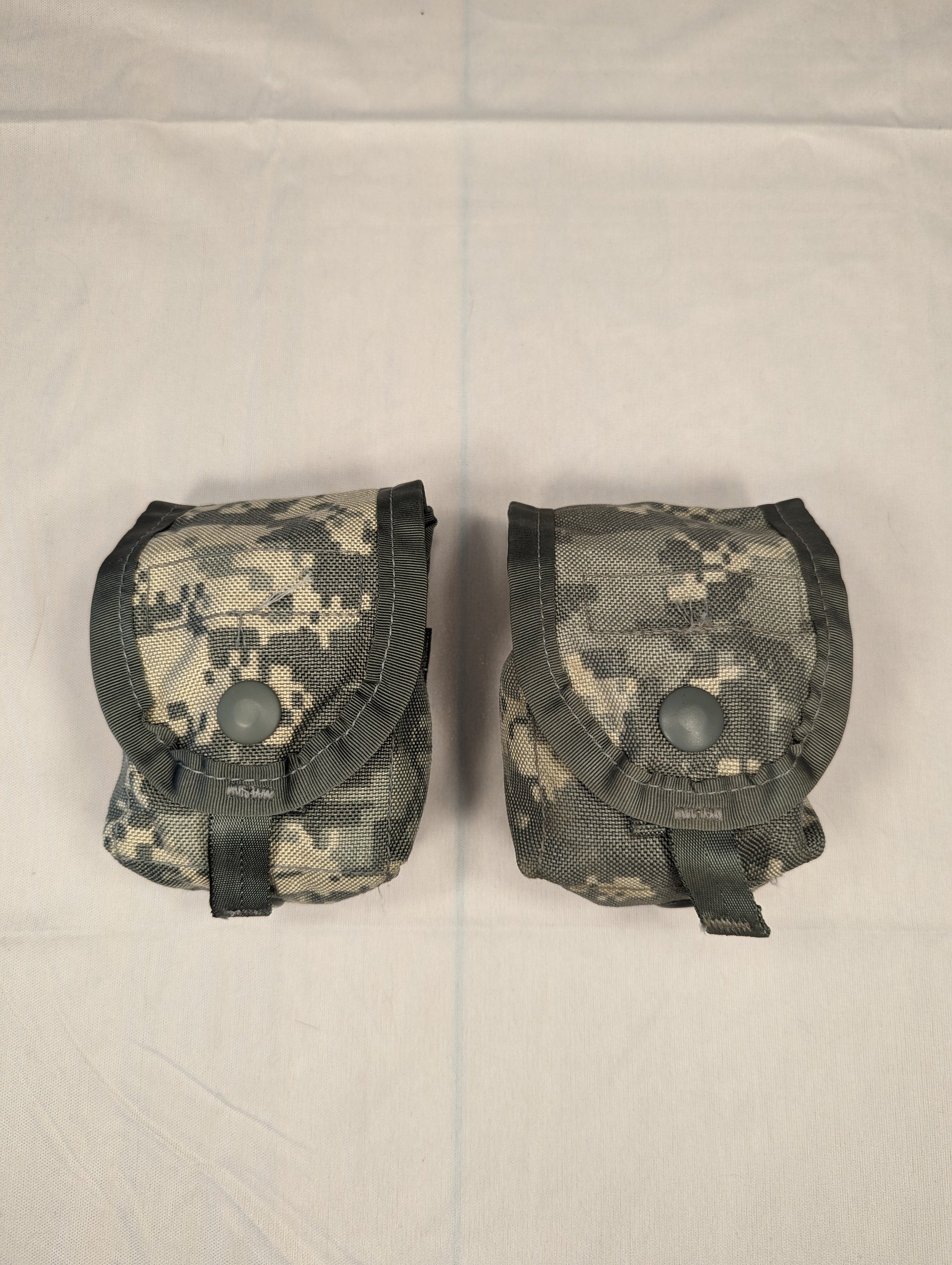 A close-up studio shot of two U.S. Military Surplus Hand Grenade Pouches in ACU digital camouflage, shown side-by-side, highlighting their box-like shape and secured snap-button flaps.