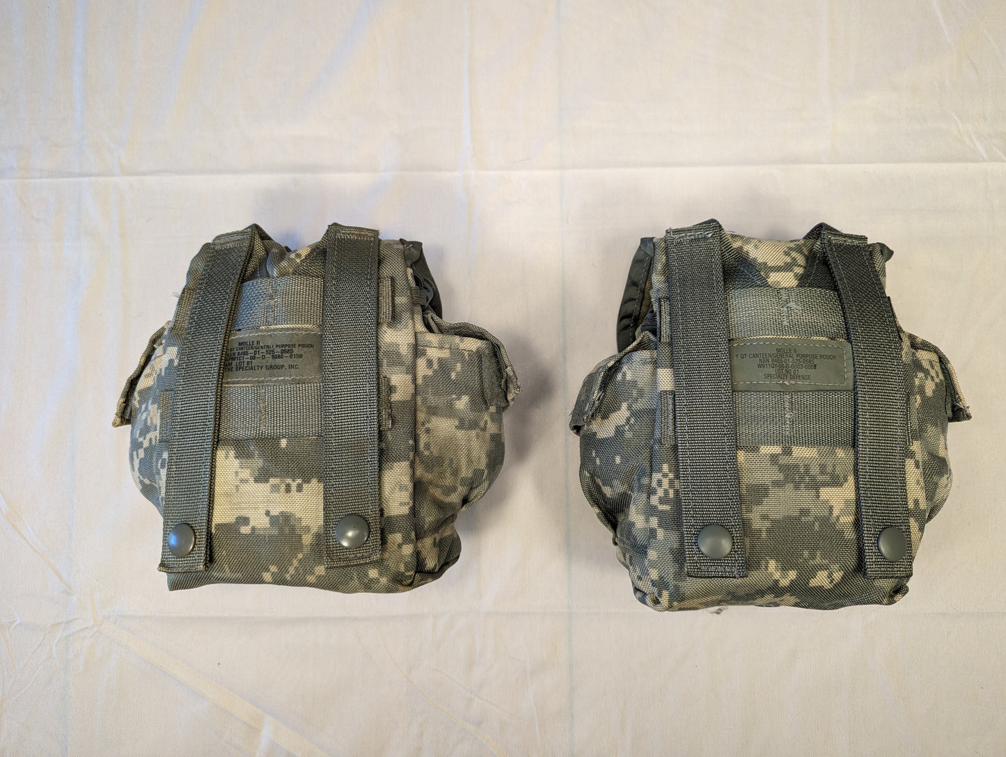 A studio shot of two U.S. Military Surplus Hand Grenade Pouches in ACU digital camouflage, shown side-by-side, featuring a snap-button flap and a central manufacturer's tag on each pouch.