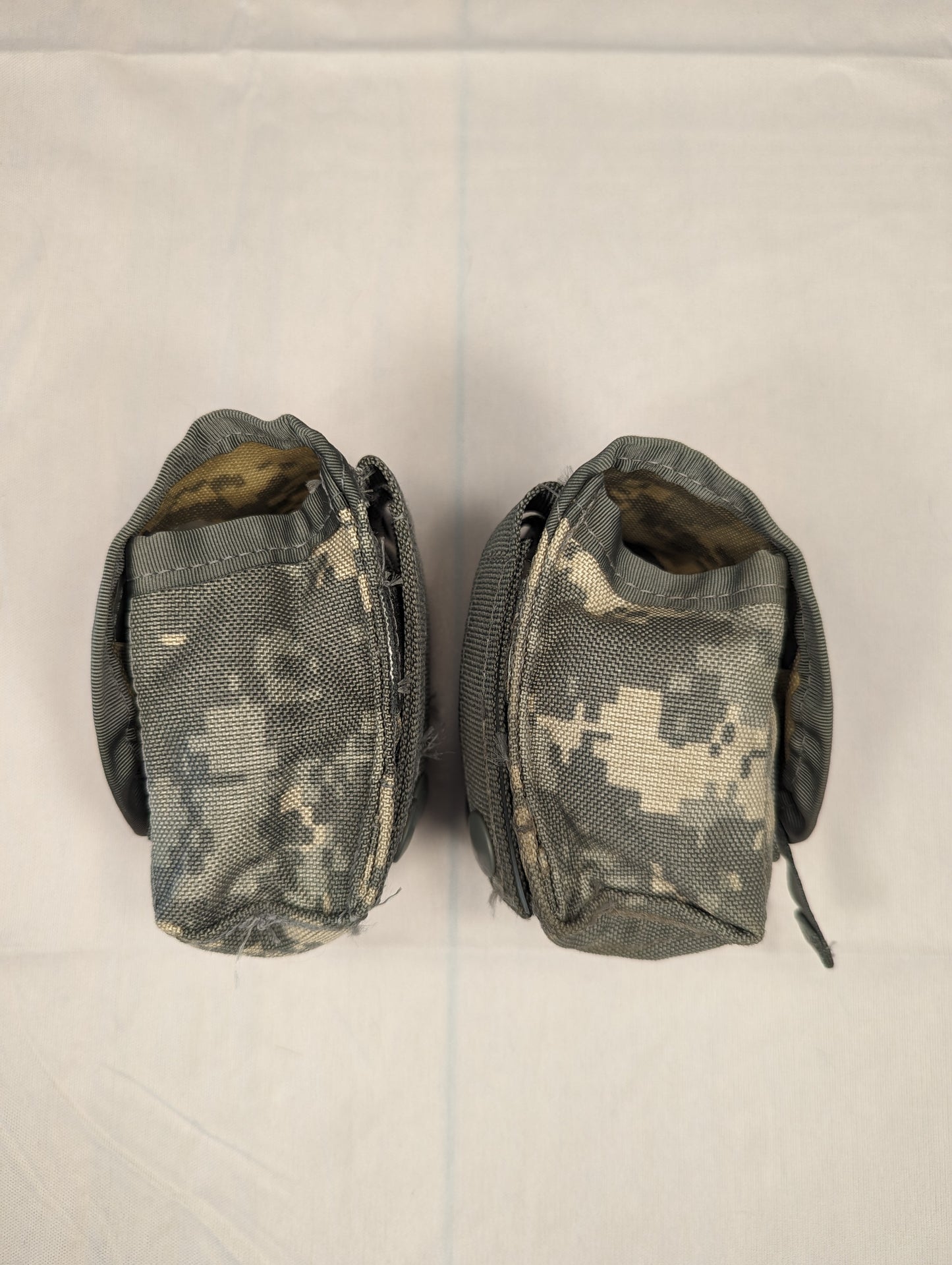 A close-up studio shot of two U.S. Military Surplus Hand Grenade Pouches in ACU digital camouflage, standing upright with the top flaps partially open, revealing the empty, padded interior.