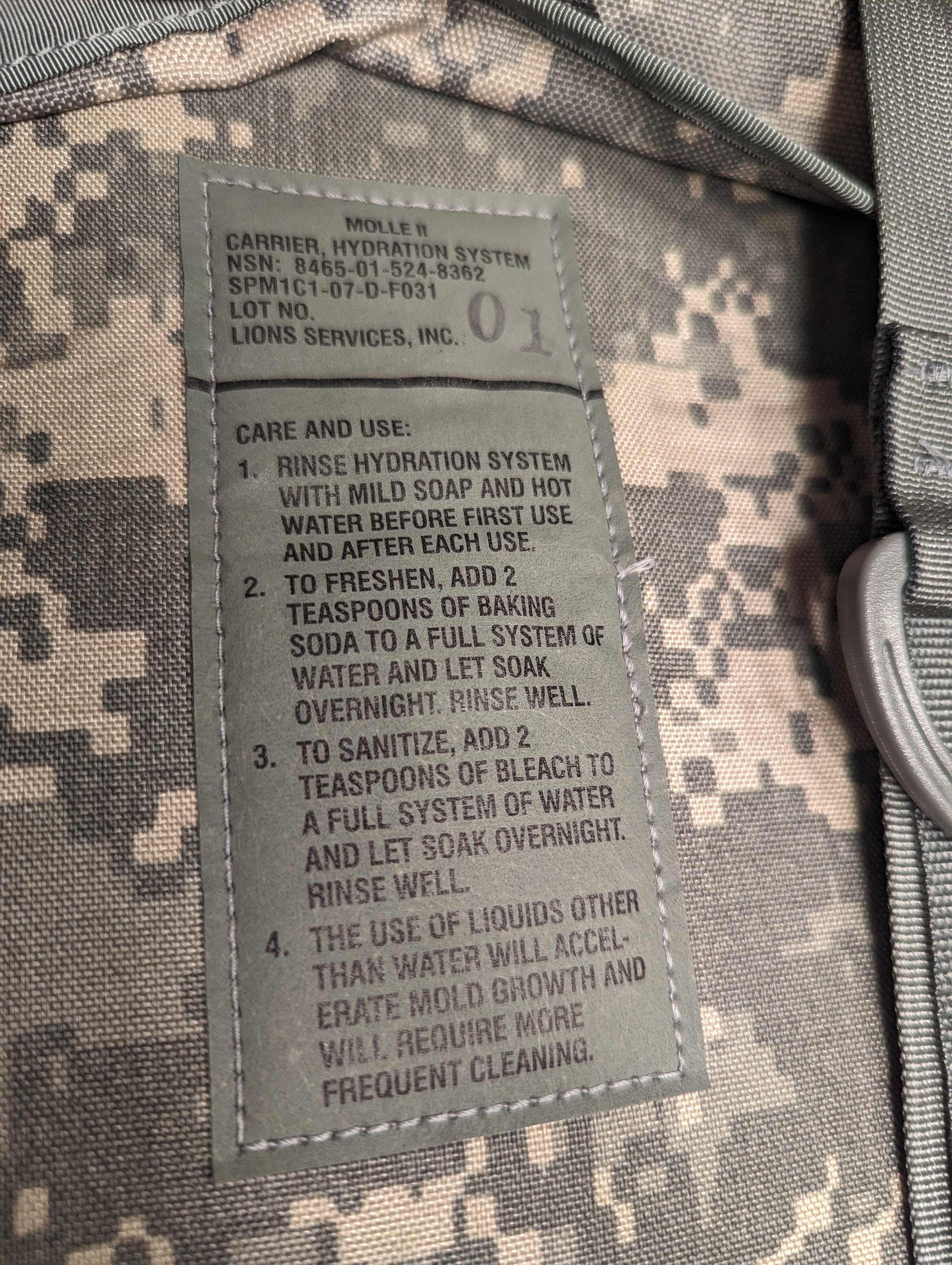 A close-up photograph of the U.S. Military Hydration Carrier care tag, displaying detailed cleaning and sanitizing instructions using mild soap, baking soda, and bleach, with a mold warning.