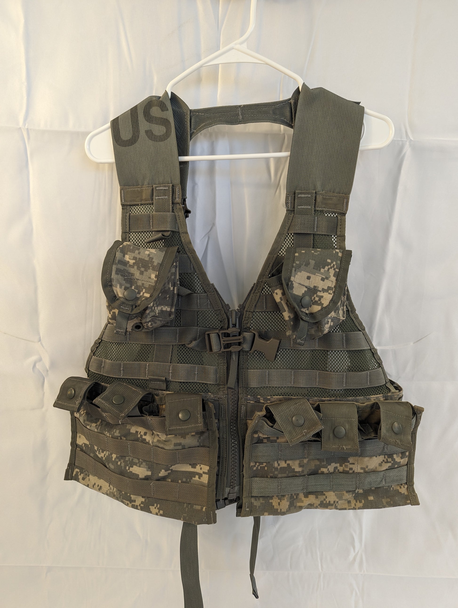 A U.S. Military Surplus Load Carrier Vest (FLC) in ACU digital camouflage, fully assembled with two double magazine pouches and two grenade pouches, hanging on a white hanger for display.