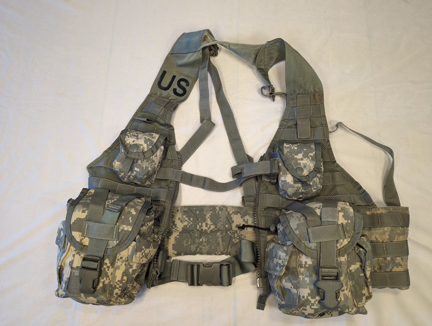 A U.S. Military Surplus Load Carrier Vest (FLC) in ACU digital camouflage, fully assembled with attached magazine and grenade pouches, laid flat, and featuring the stenciled 'US' mark on the shoulder.