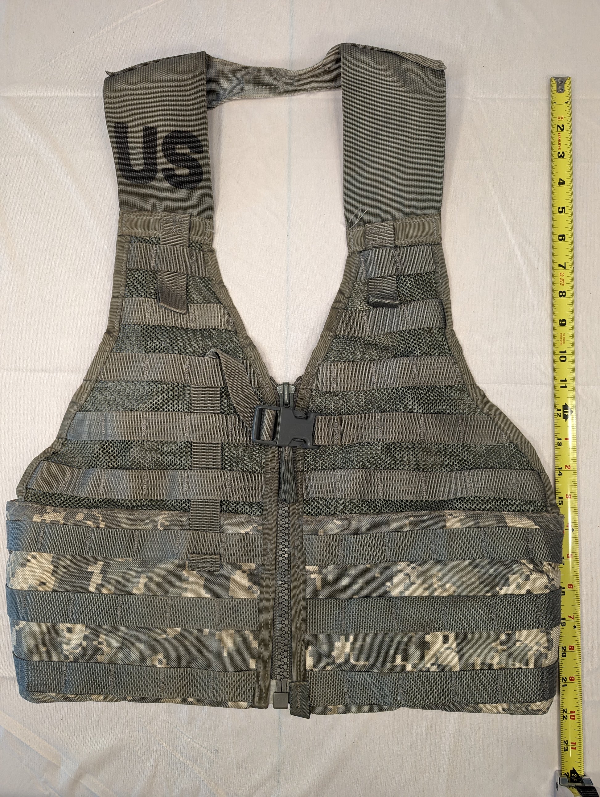 A full front view of a U.S. Military Surplus Load Carrier Vest (FLC) in ACU digital camouflage, unaccessorized, laid flat with a tape measure showing its vertical height, highlighting the extensive MOLLE webbing.