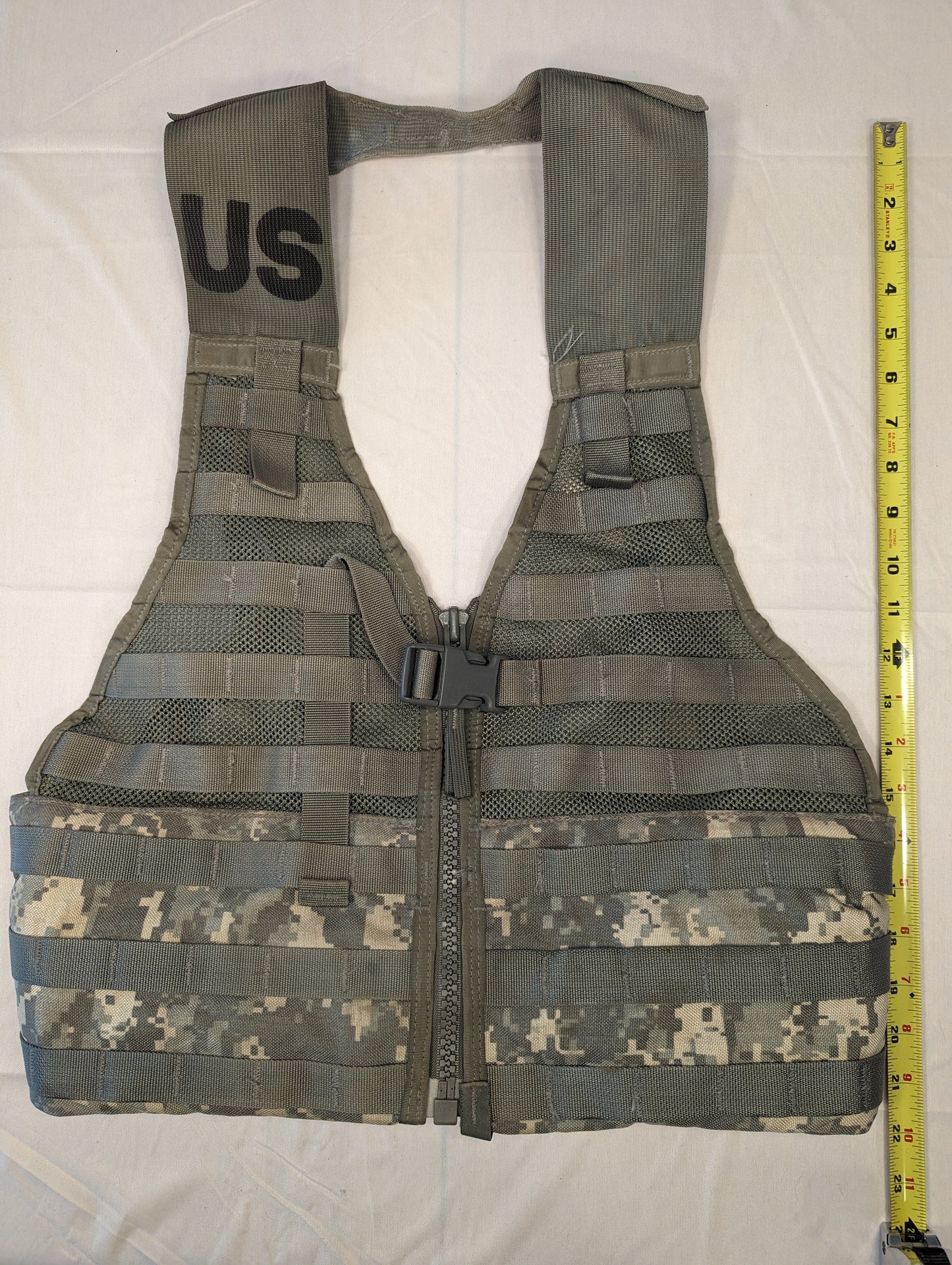 A U.S. Military Surplus Load Carrier Vest (FLC) in ACU digital camouflage, unaccessorized, laid flat with a tape measure showing its vertical height, highlighting the extensive MOLLE webbing.