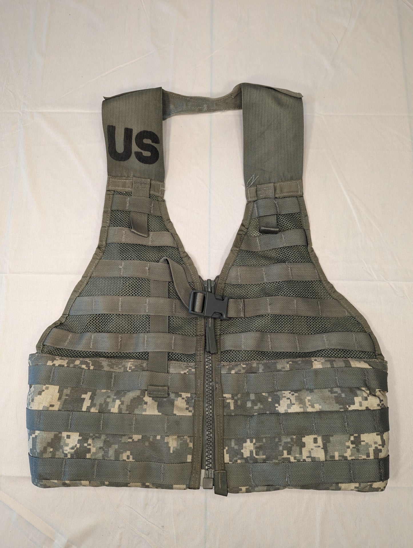 A full front view of a U.S. Military Surplus Load Carrier Vest (FLC) in ACU digital camouflage, unaccessorized, displaying the extensive horizontal MOLLE webbing and the stenciled 'US' government marking on the shoulder.