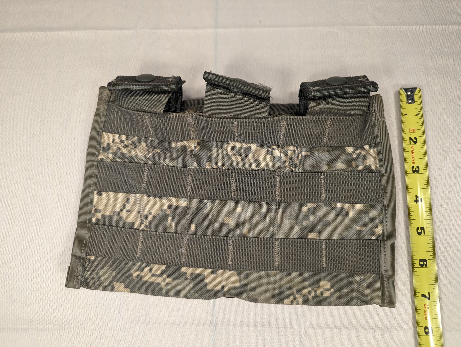 A single U.S. Military Surplus Triple Magazine Pouch in ACU digital camouflage, laid flat with a tape measure showing its height, highlighting the dense horizontal MOLLE webbing and three visible magazine slots.