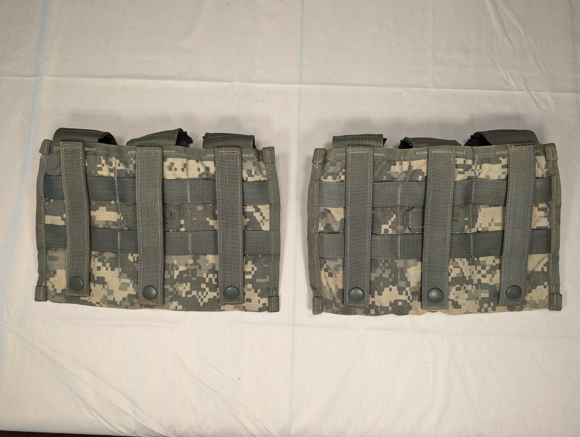 A close-up studio shot of two U.S. Military Surplus Triple Magazine Pouches in ACU digital camouflage, laid side-by-side, featuring dense horizontal MOLLE webbing and snap-button flaps.
