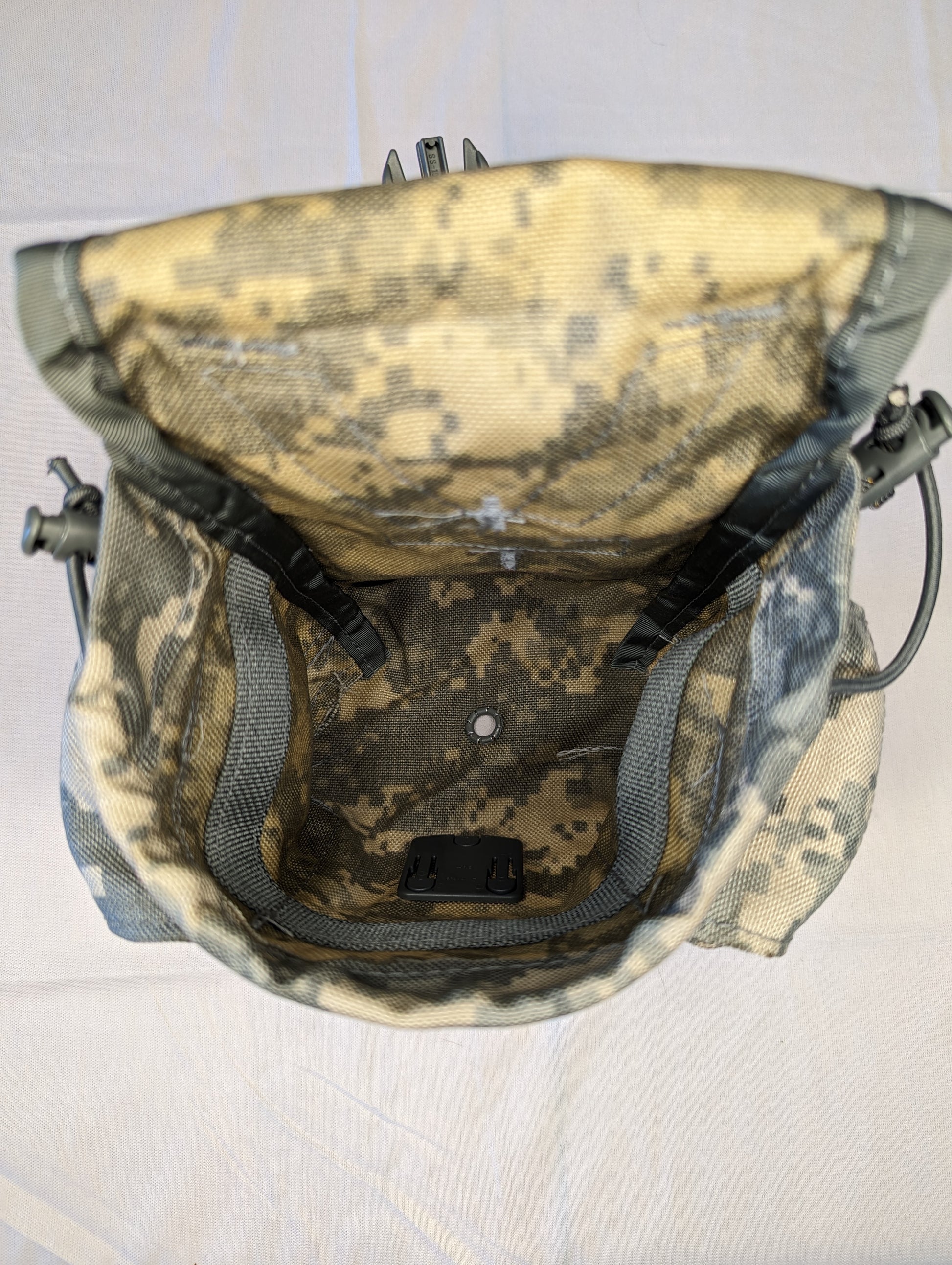 A close-up, high-angle view looking deep inside the empty ACU digital camouflage utility pouch, showing the dark mesh lining, internal features, and drawstring collar.