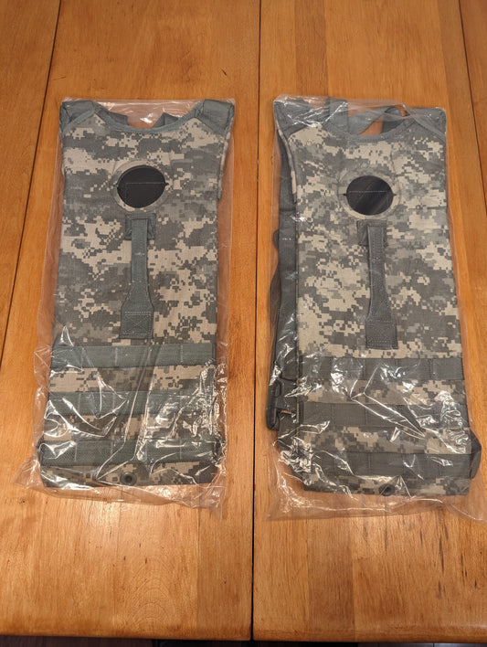 Two new U.S. Military Surplus Hydration Carriers in ACU/UCP digital camouflage, sealed in clear plastic packaging, showing the pattern and filler port on a wooden background.