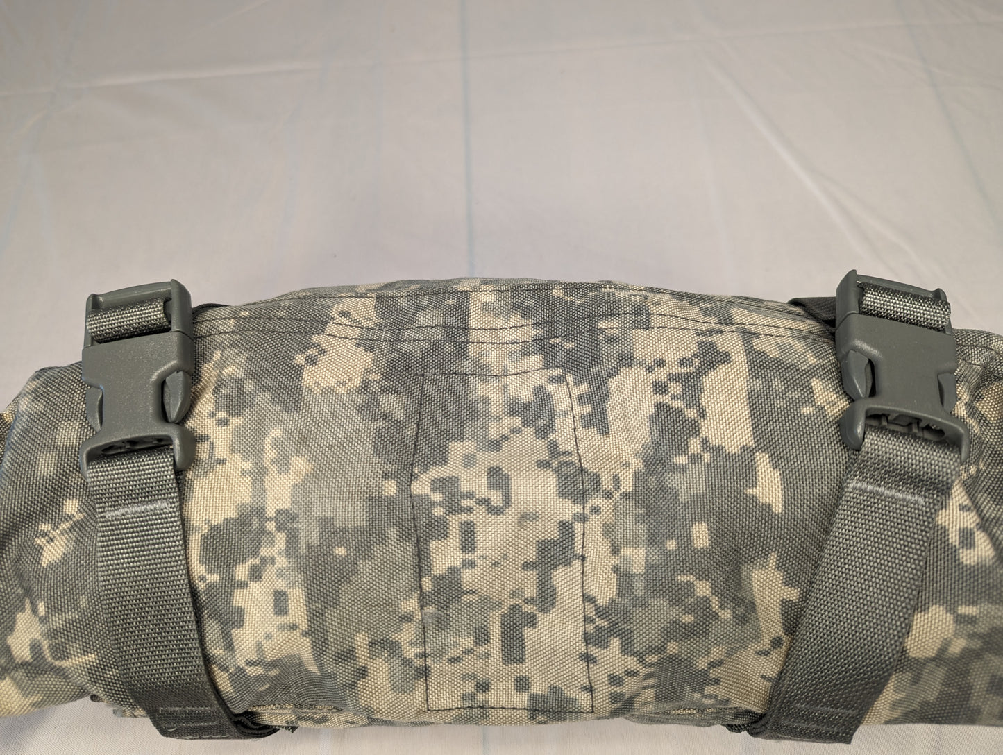 A close-up view of a U.S. Military Surplus Waist Pack in ACU digital camouflage, tightly rolled and secured by two horizontal webbing straps with black quick-release buckles.