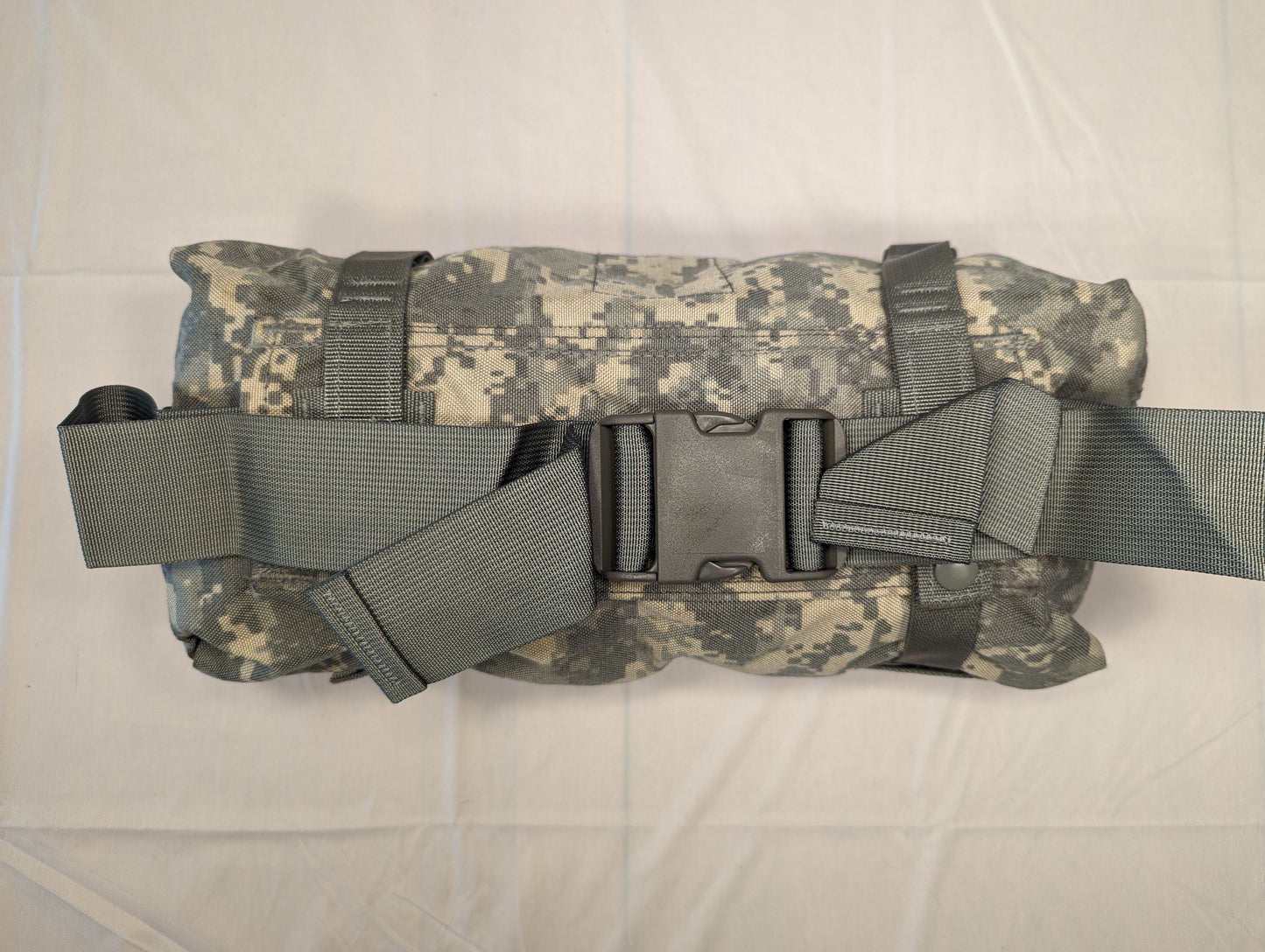 A U.S. Military Surplus Waist Pack in ACU digital camouflage, tightly rolled and secured by wide gray webbing compression straps fastened with a black quick-release buckle.