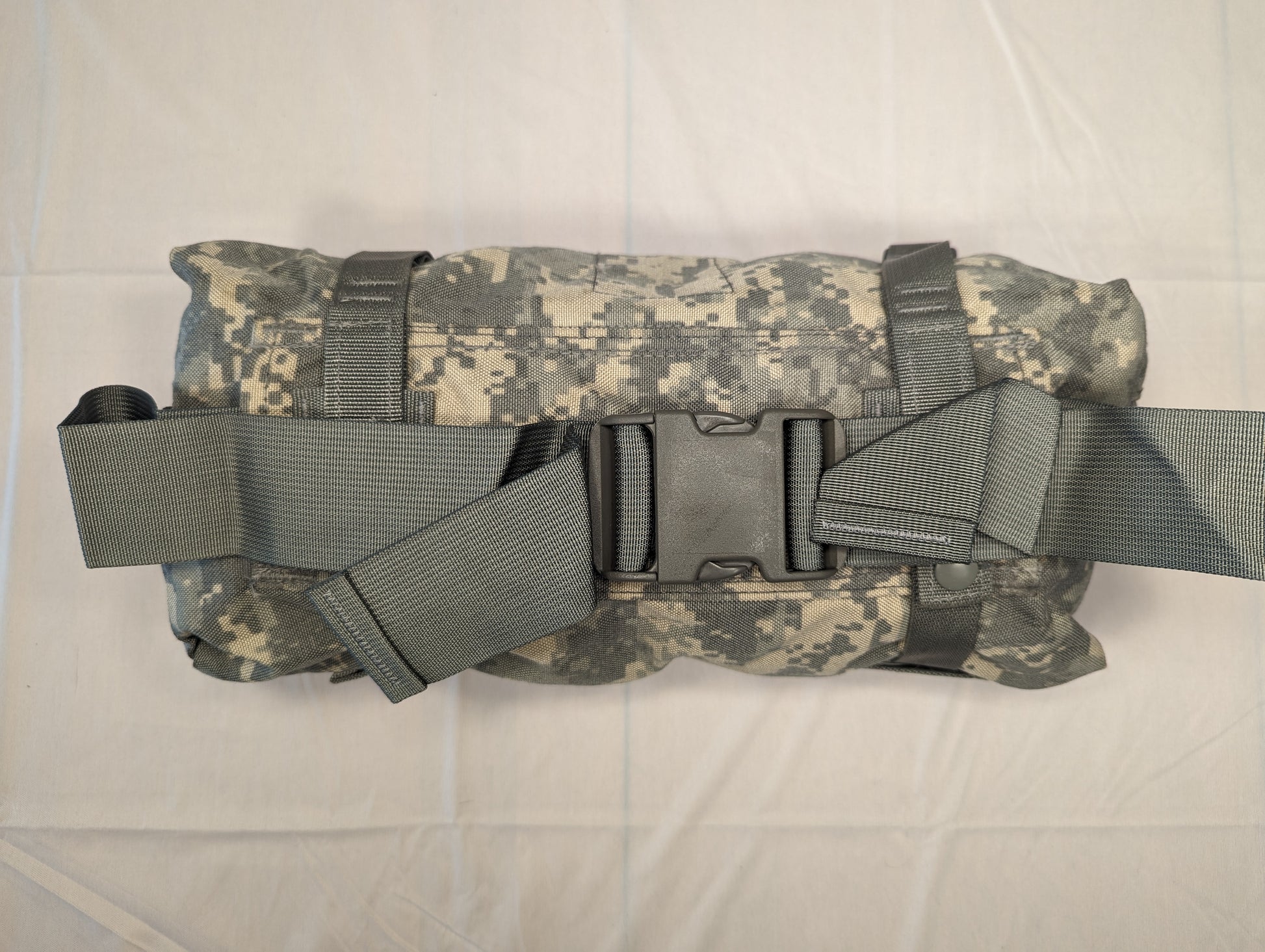 A U.S. Military Surplus Waist Pack in ACU digital camouflage, tightly rolled and secured by wide gray webbing compression straps fastened with a black quick-release buckle.