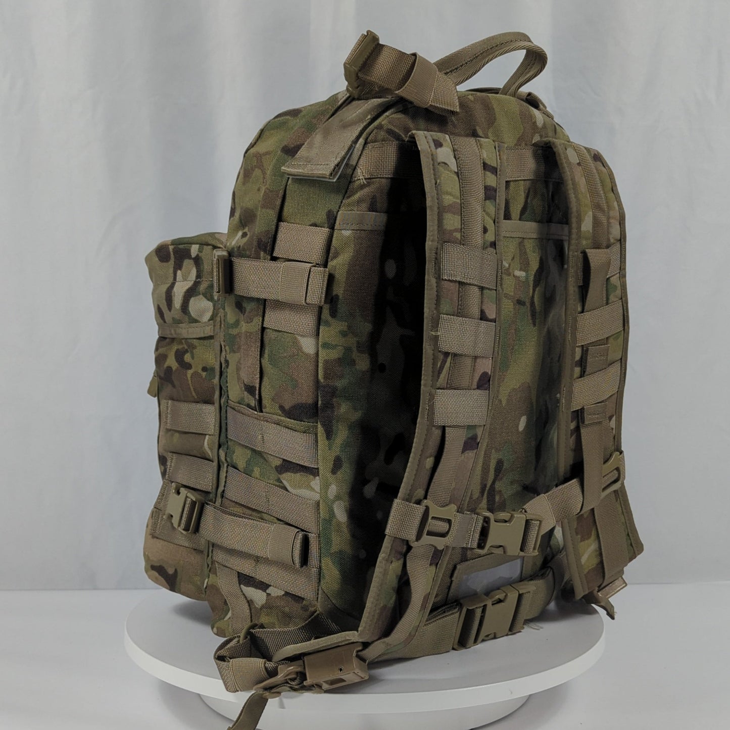 A back view of a U.S. Military Assault Pack in OCP/Multicam camouflage, highlighting the padded shoulder harness, hip belt, and PALS/MOLLE webbing attachment points.
