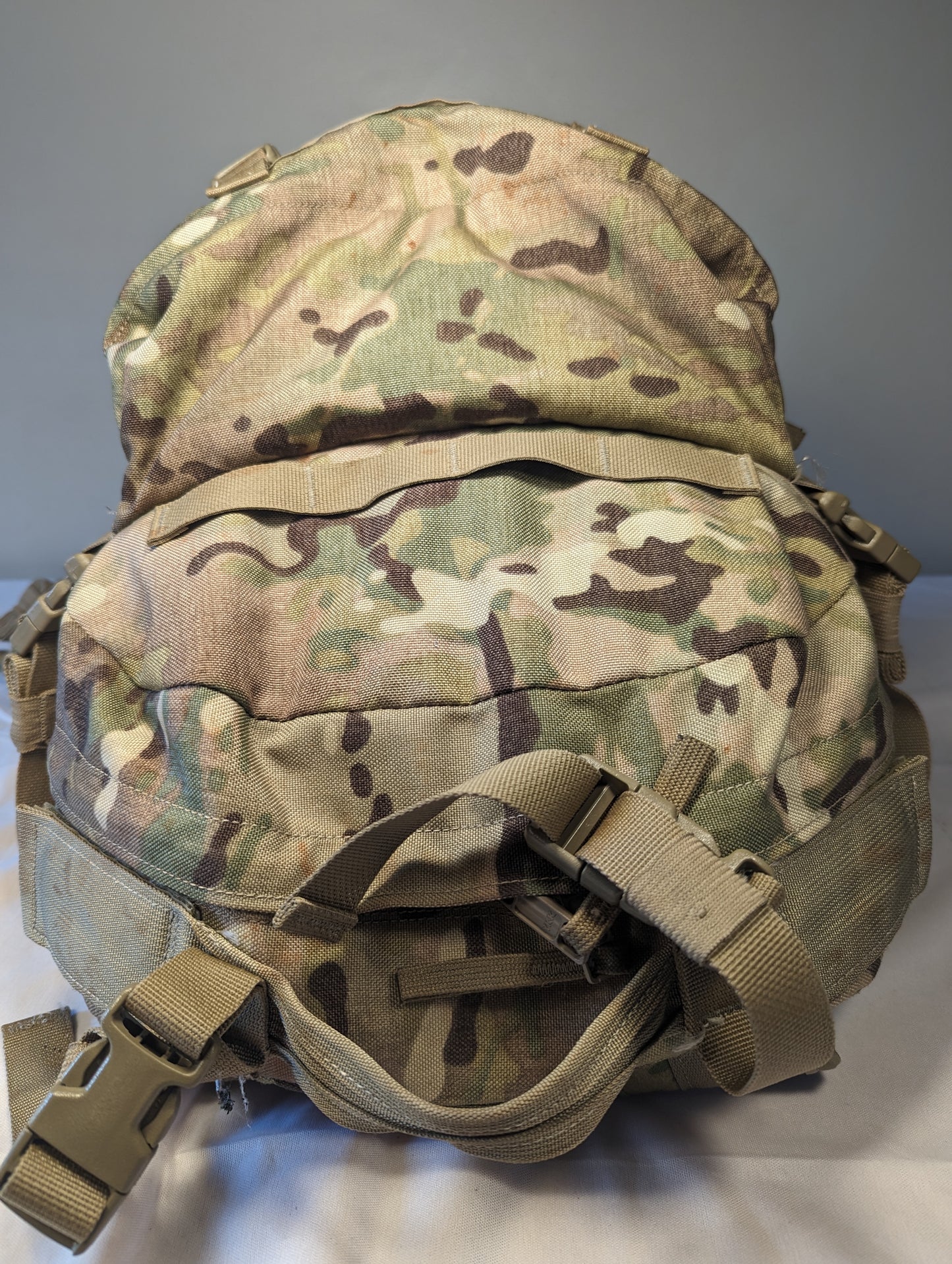 A rear view of a U.S. Military Surplus Assault Pack in OCP/Multicam camouflage, showing the padded back panel, horizontal MOLLE webbing, carry handle, and adjustable shoulder strap buckles.